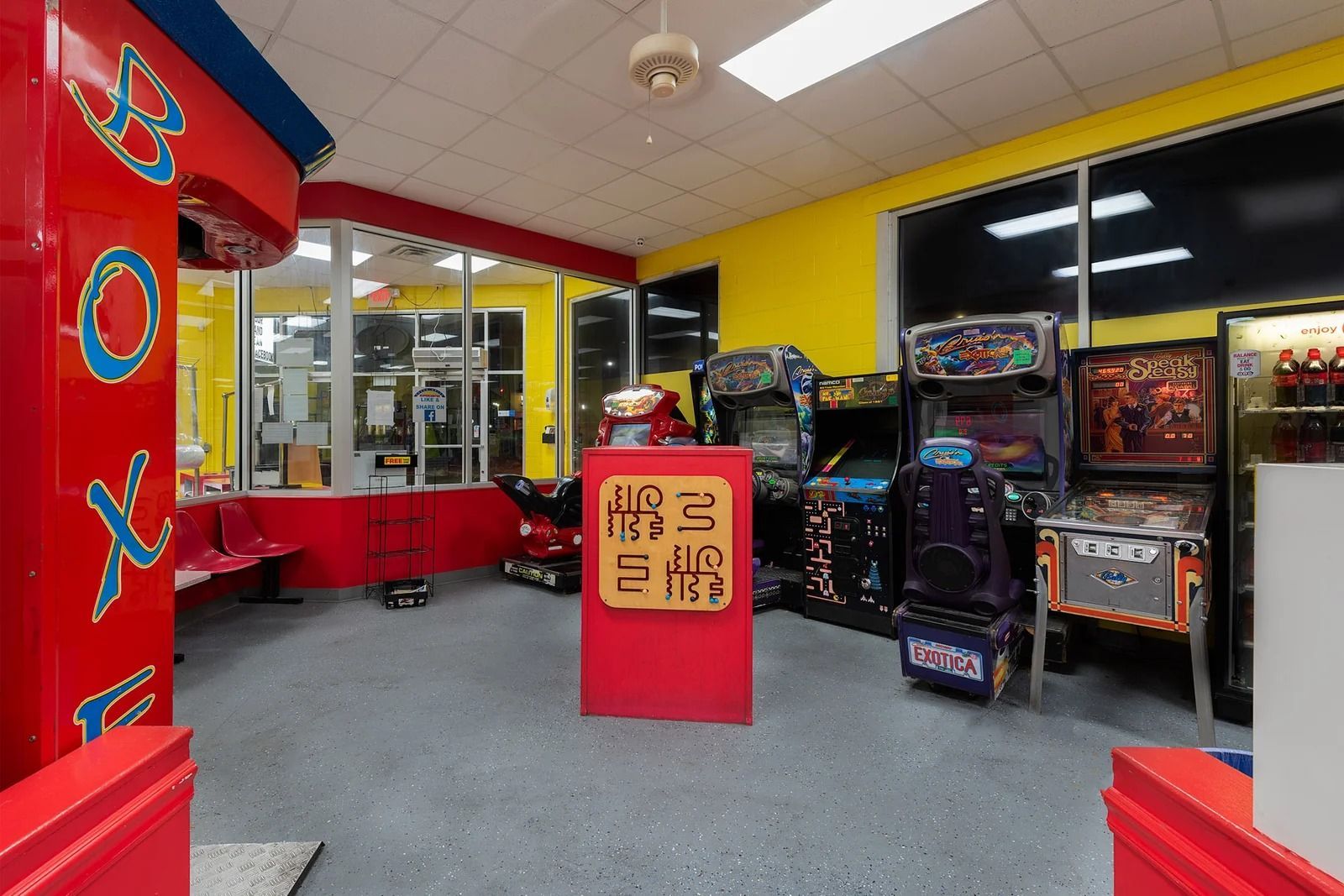 Arcade interior with red and yellow walls, lit by overhead lighting. Arcade games line the walls.