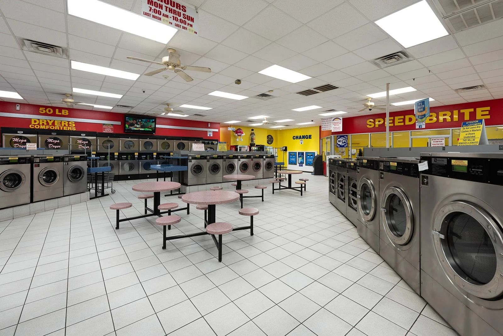 A laundromat interior with rows of washing machines, tables, and bright fluorescent lights.