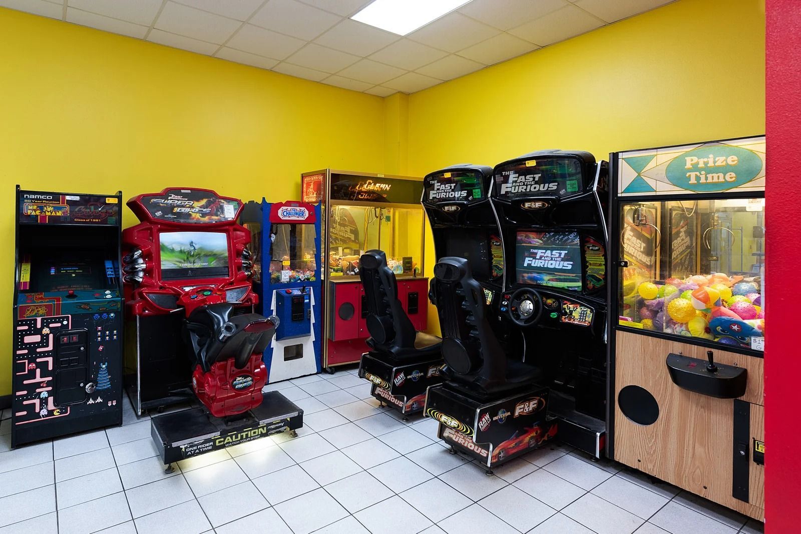Arcade with several gaming machines; yellow walls, white tile floor.