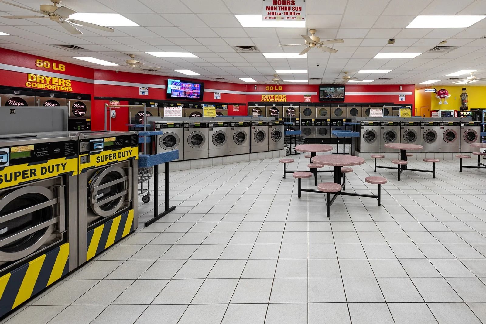 Interior view of a laundromat with rows of washers and dryers, tables, and red and yellow accents.