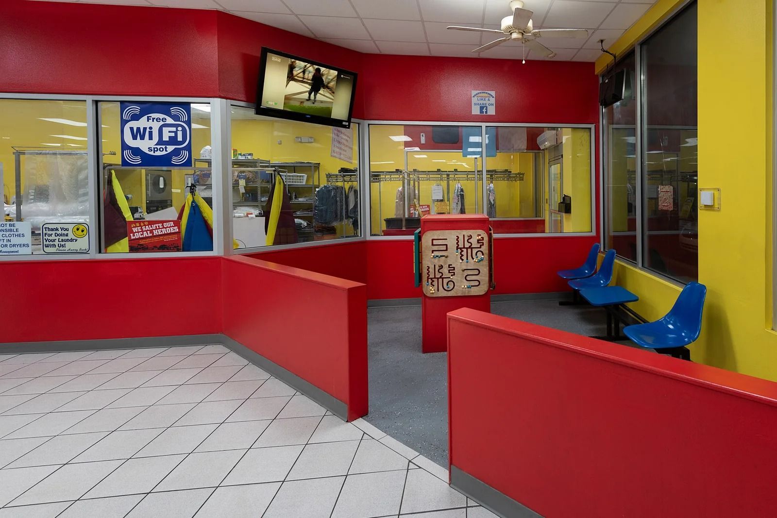Red and yellow laundromat interior with windows, TV, seating, and Wi-Fi sign.