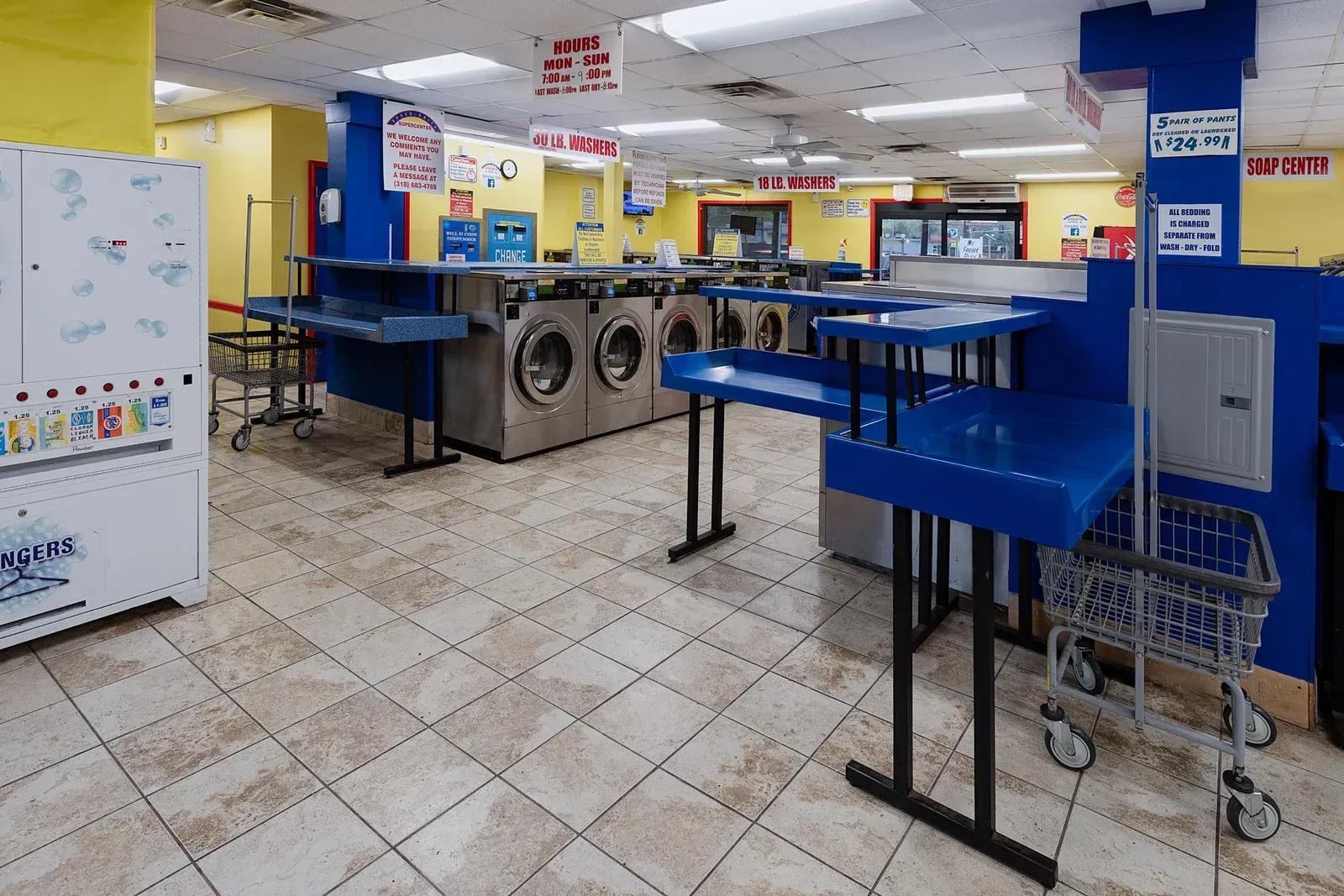 Interior view of a laundromat with washers, folding tables, and a shopping cart.