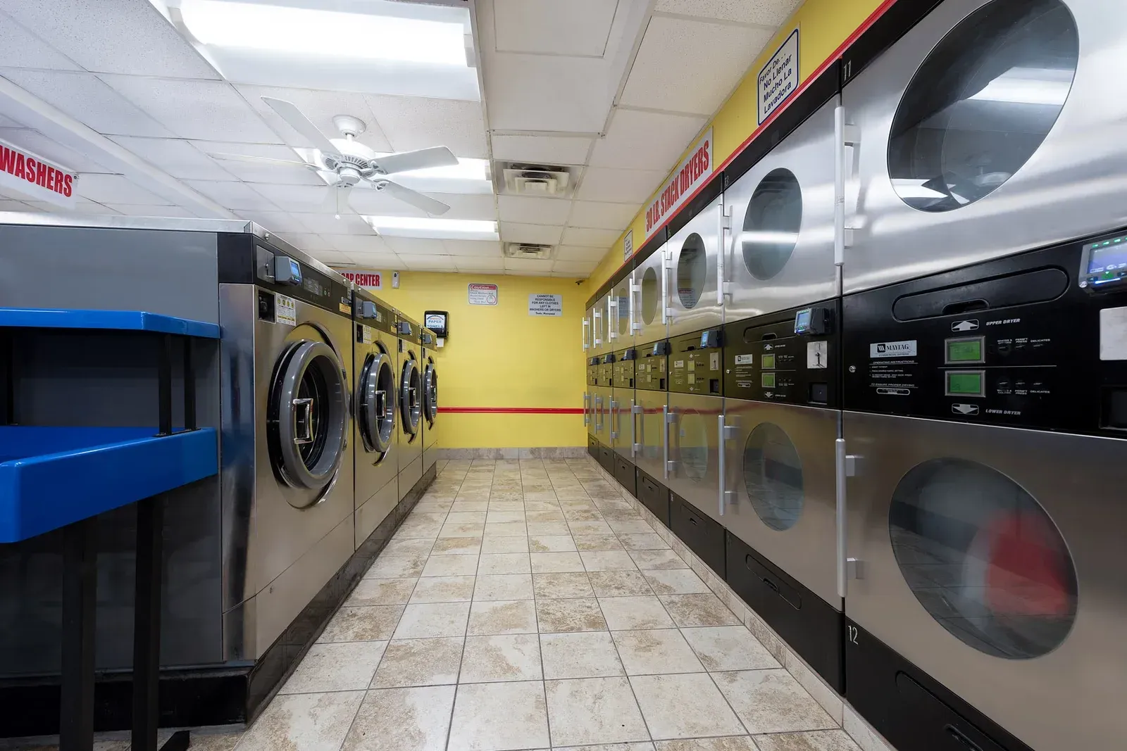 Rows of washing machines in a laundromat with yellow walls and tile floor.