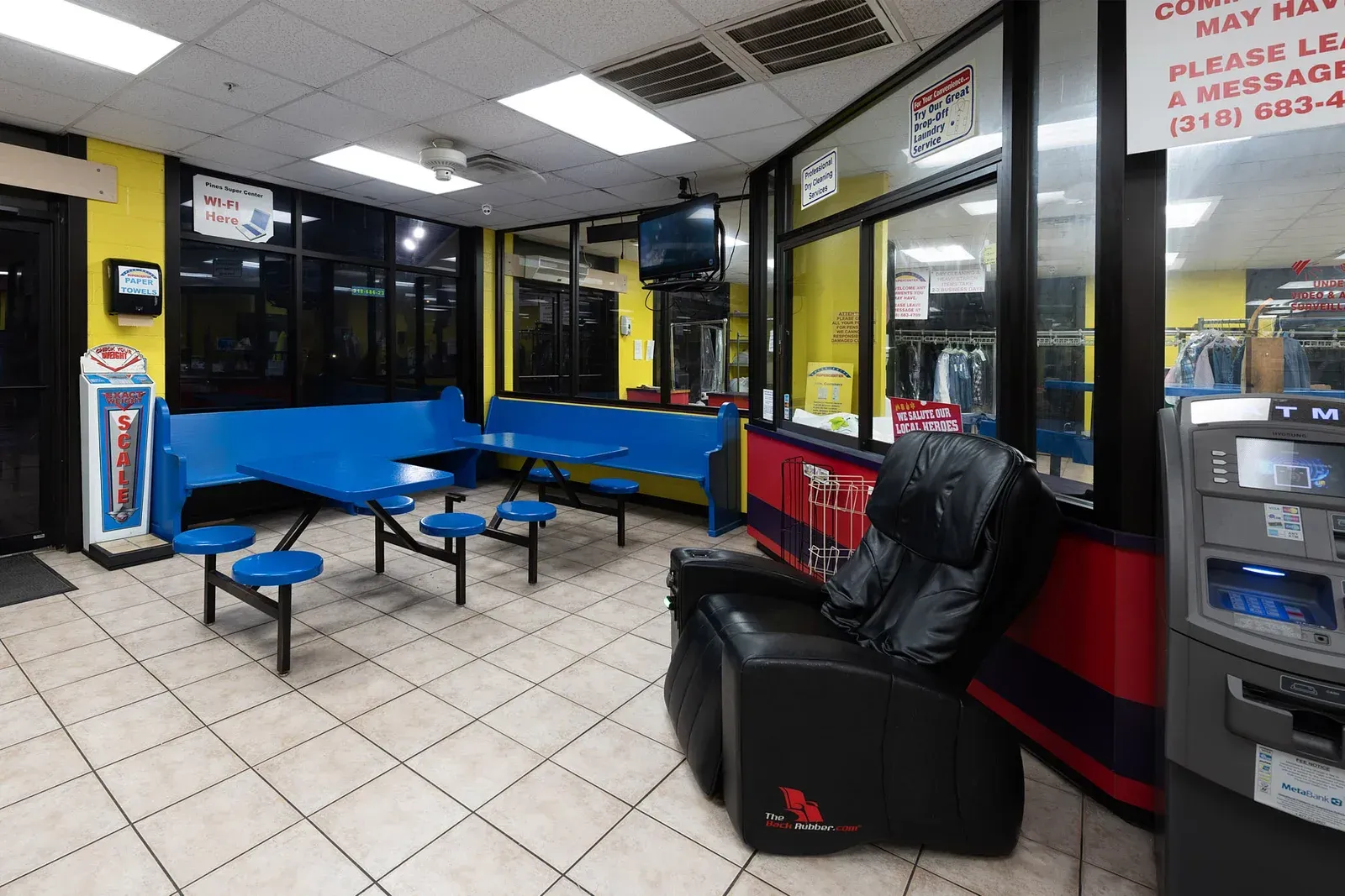 Waiting area with blue benches, a massage chair, and a view of the service bays.