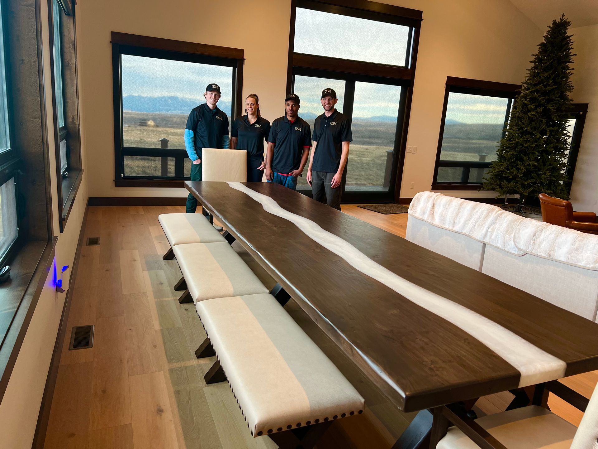 A group of people standing around a long wooden table in a living room.