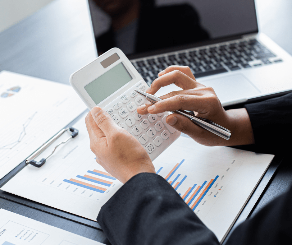 Hands using calculator, working on financial documents, laptop in background.