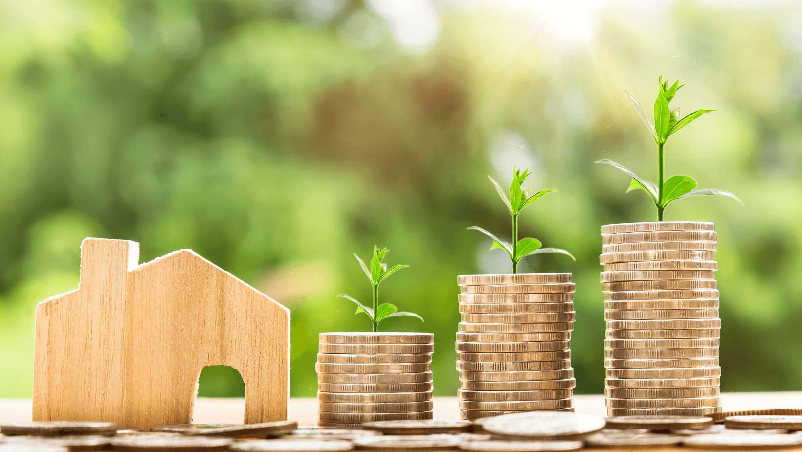 Wooden house next to stacks of coins with growing plants. Wooden house next to stacks of coins with growing plants.