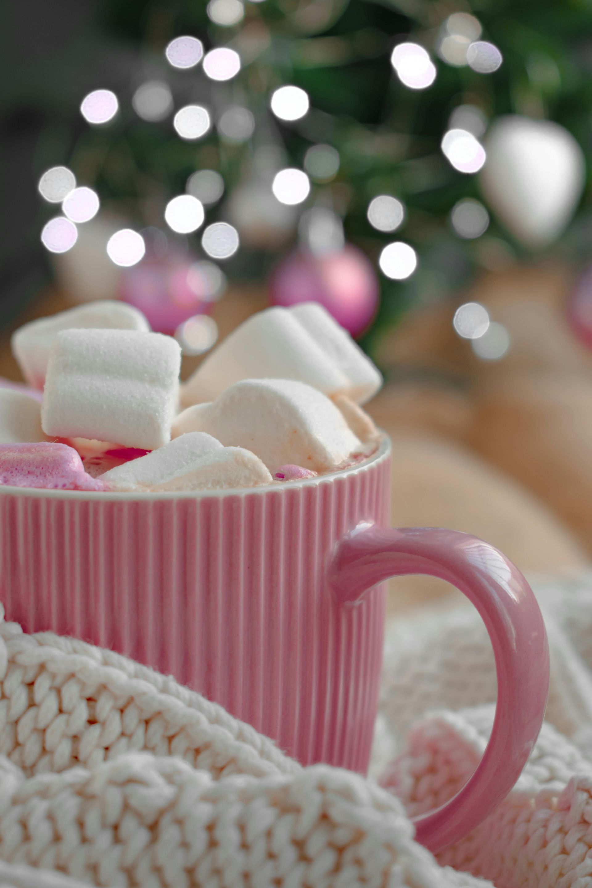 Pink mug filled with marshmallows, wrapped in a cozy cream-colored knit.