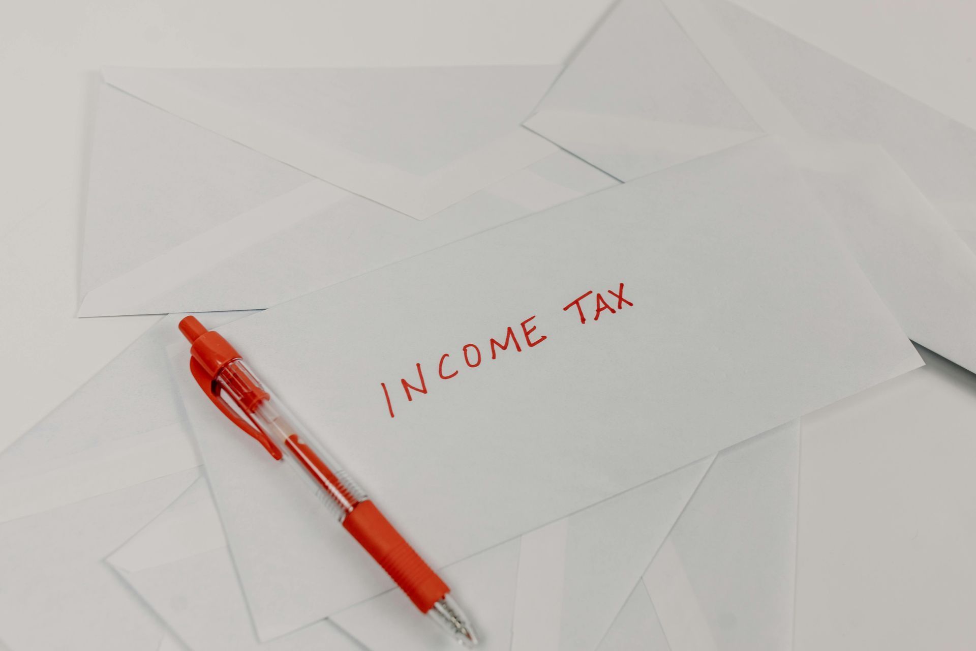 White envelopes with income tax in red, next to a red pen. White envelopes with income tax in red, next to a red pen.