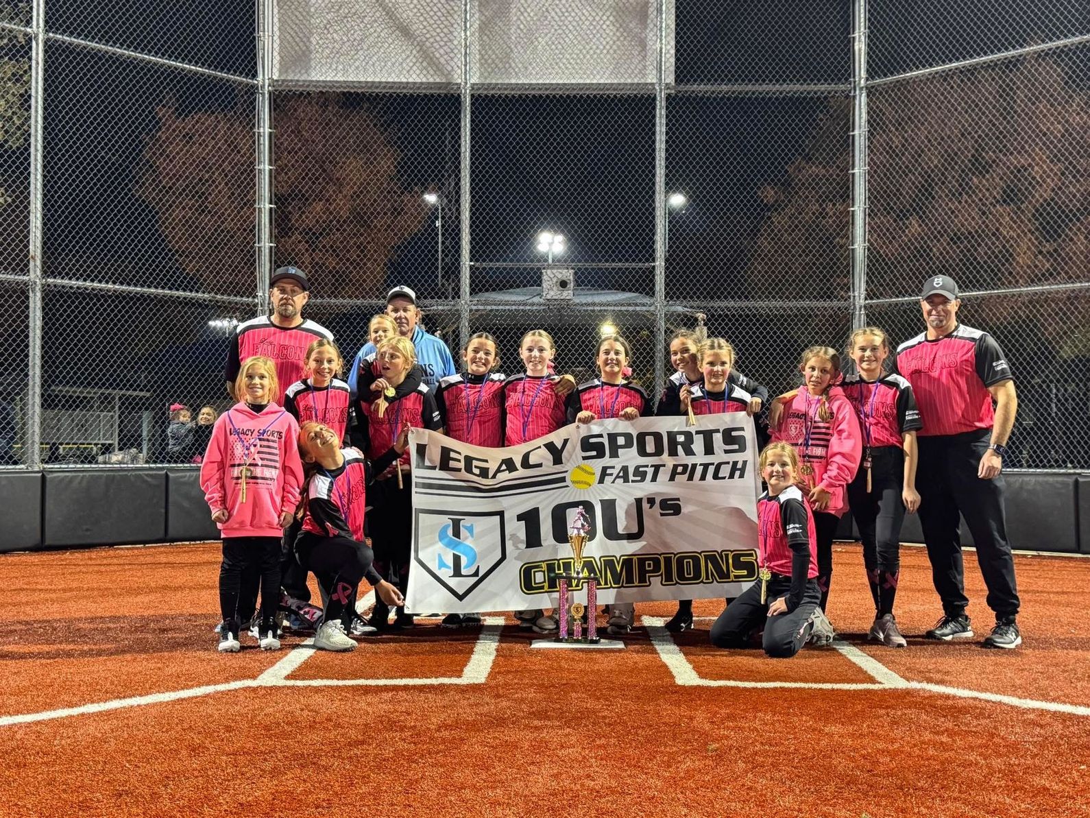 Youth baseball team posing on a red field at night with a “Legacy Sports” championship banner.
