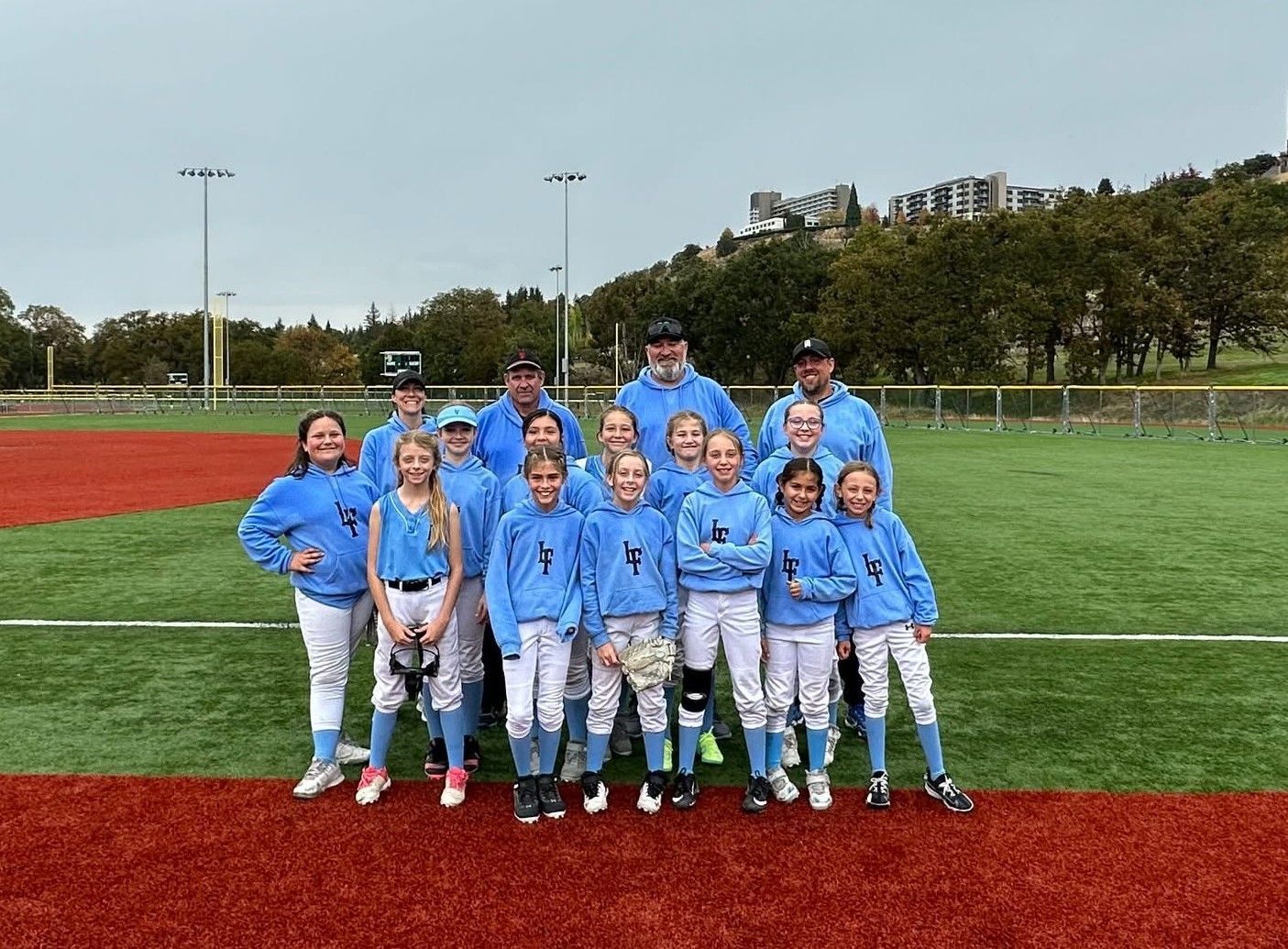 Youth baseball team in blue uniforms posing on a field with a coach, on artificial turf near a red track