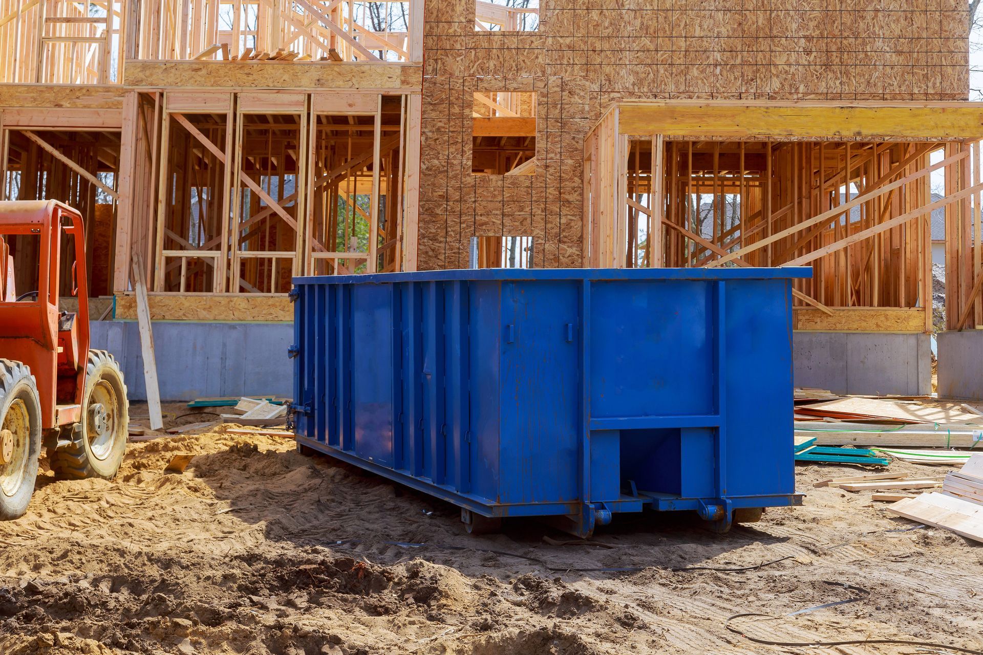 A blue dumpster is parked in front of a house under construction.