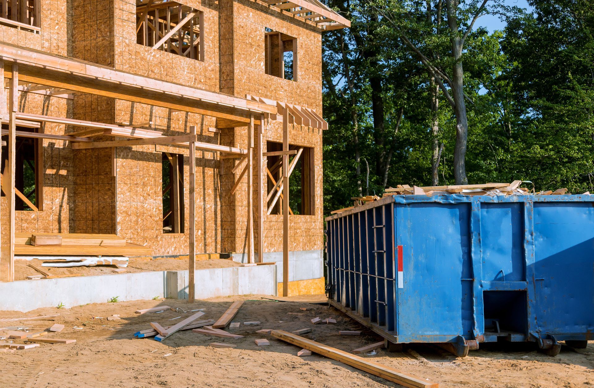 A blue dumpster is parked in front of a house under construction.