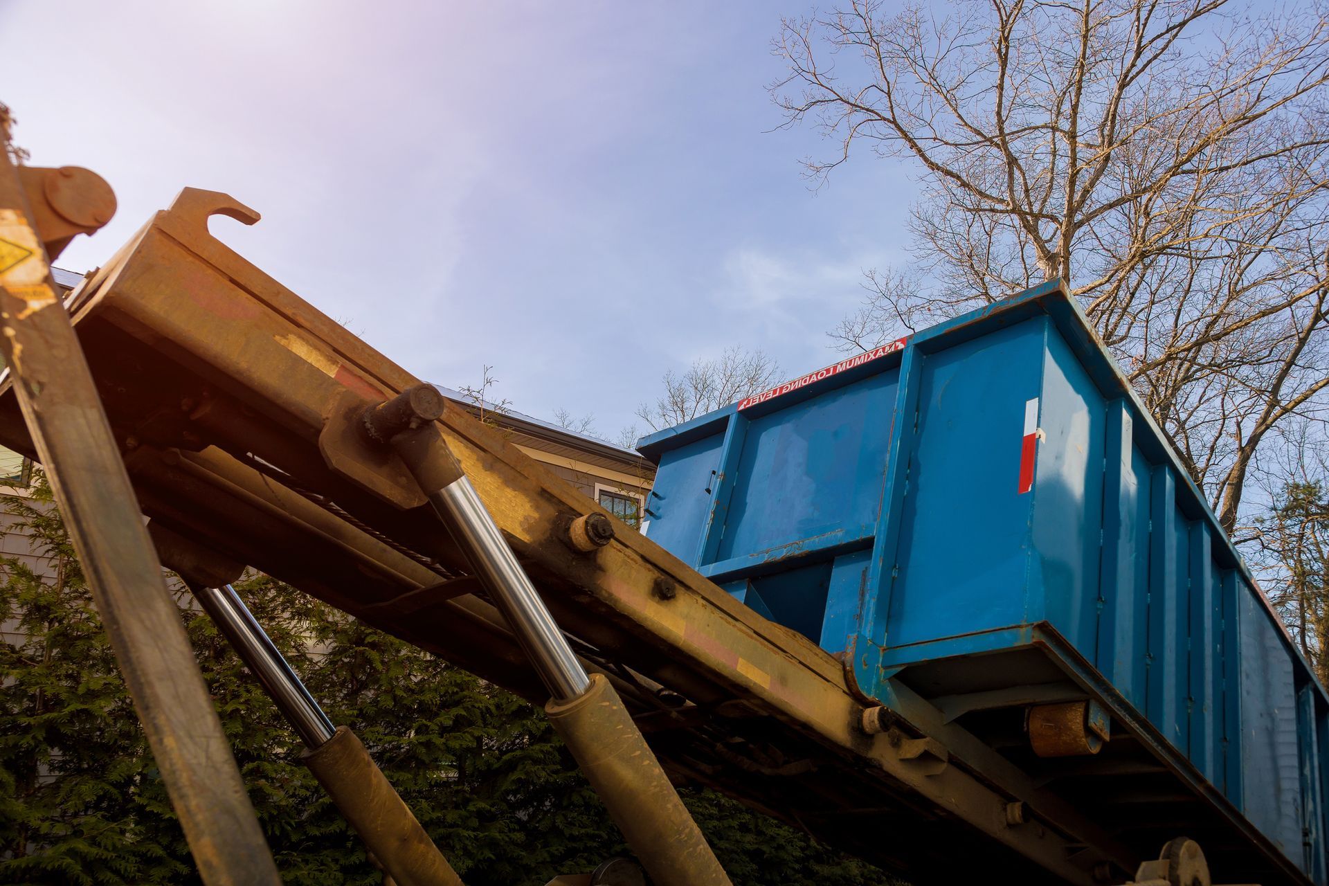 A blue dumpster is being lifted by a crane.