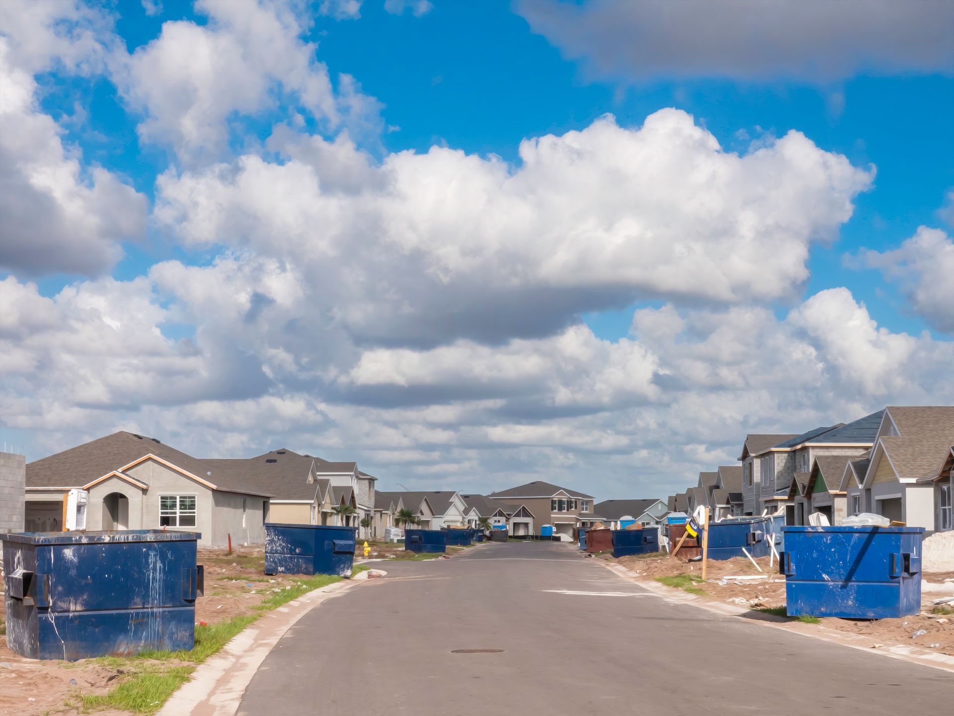A row of blue dumpsters are lined up on the side of a road in a residential neighborhood.