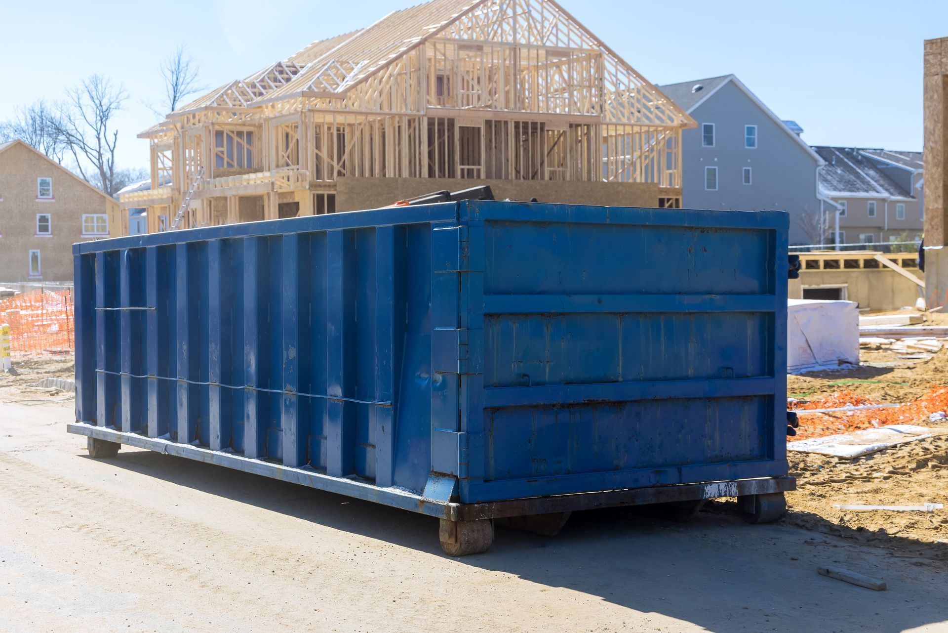 A blue dumpster is parked in front of a house under construction.