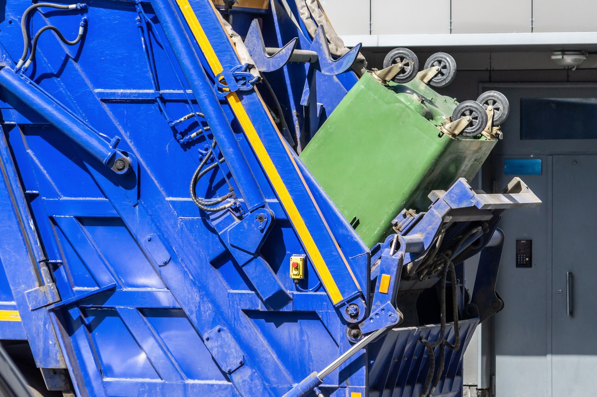 A blue garbage truck is loading a green trash can into it.