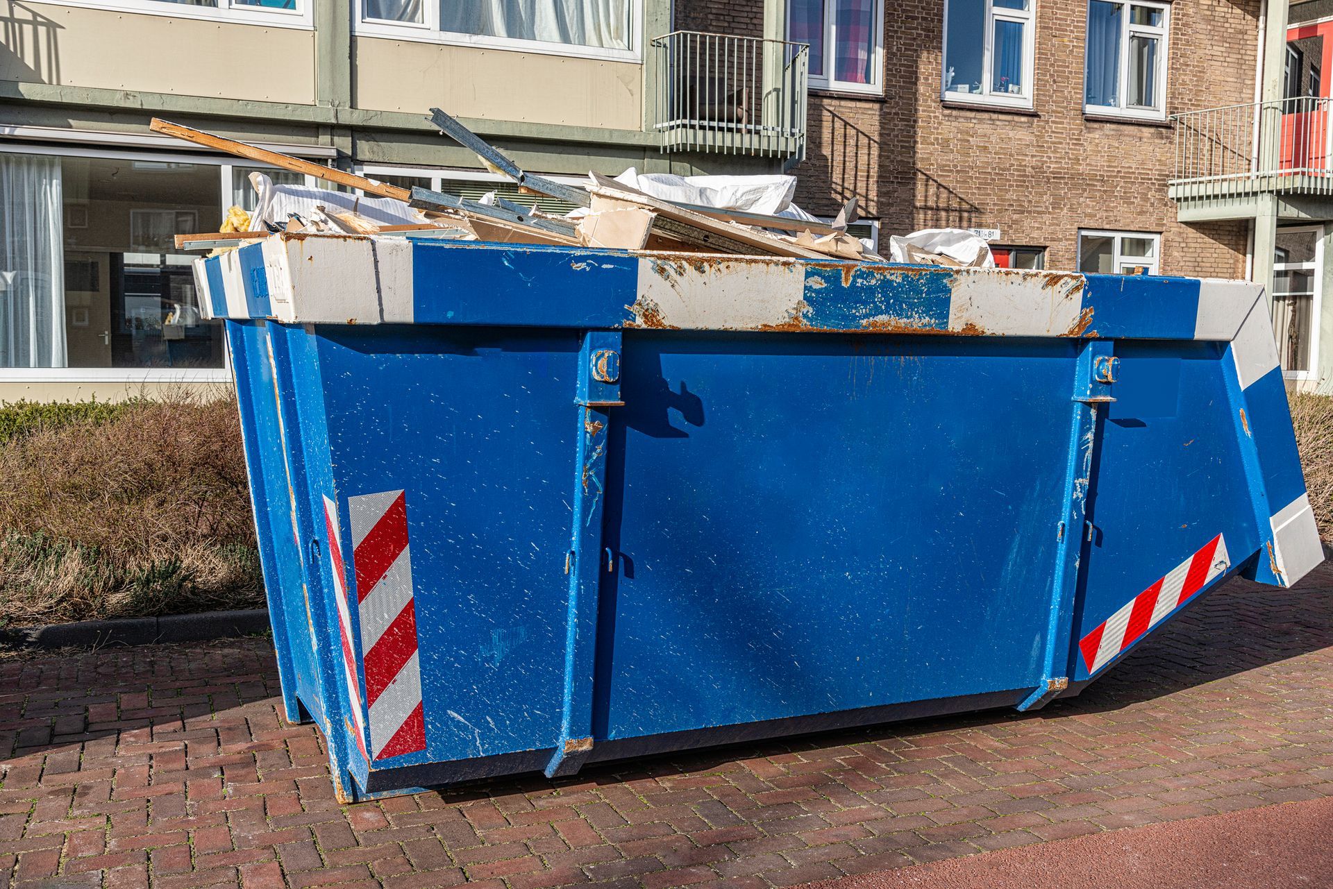 A blue dumpster is sitting on the side of the road in front of a building.
