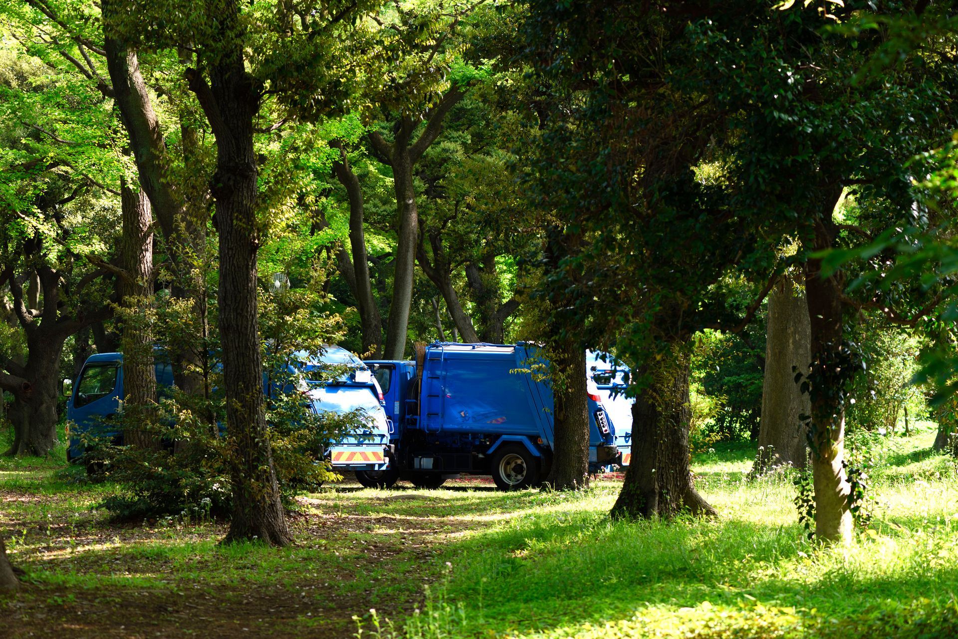 A blue garbage truck is parked in the middle of a forest.