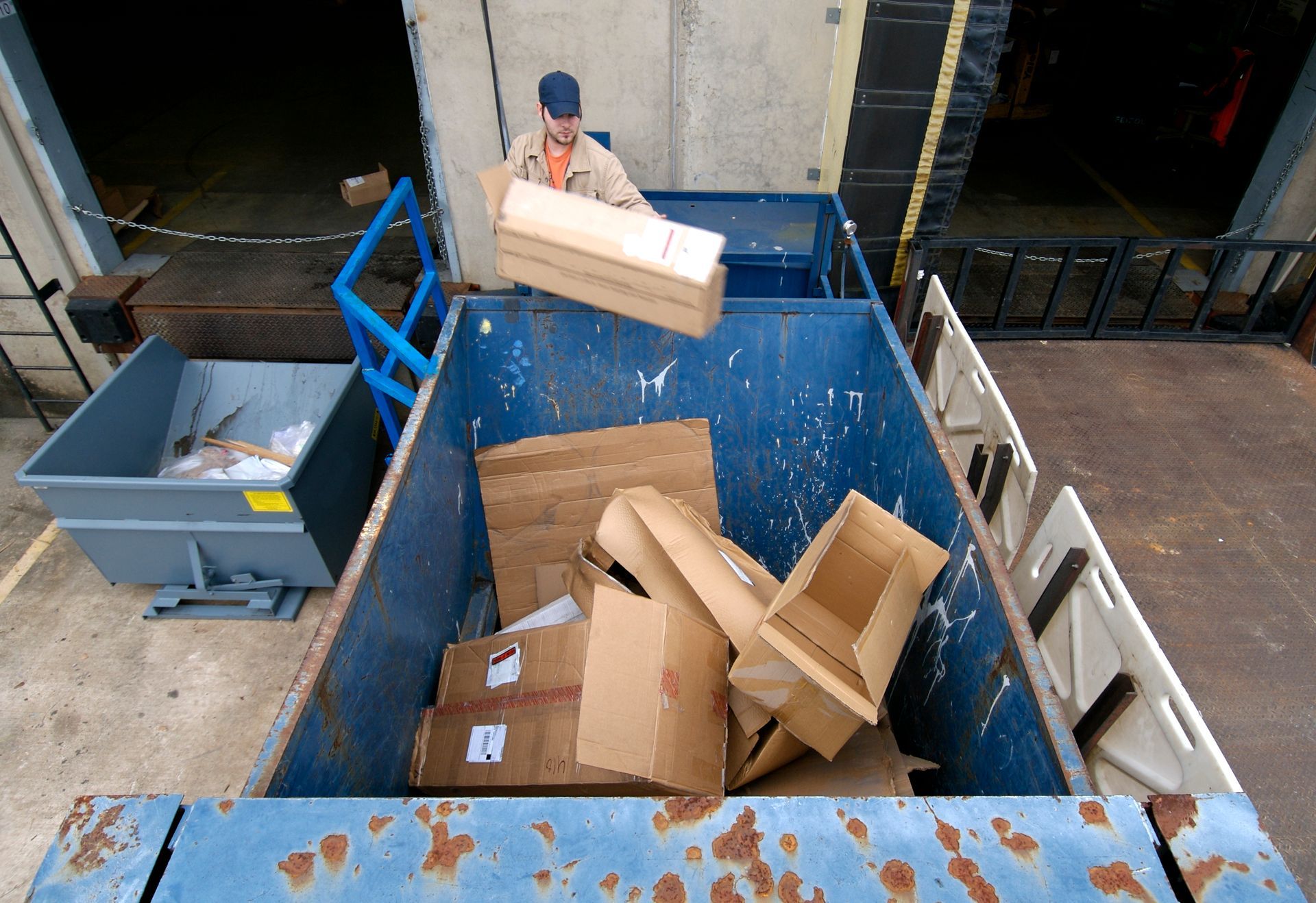 A man is loading cardboard boxes into a dumpster