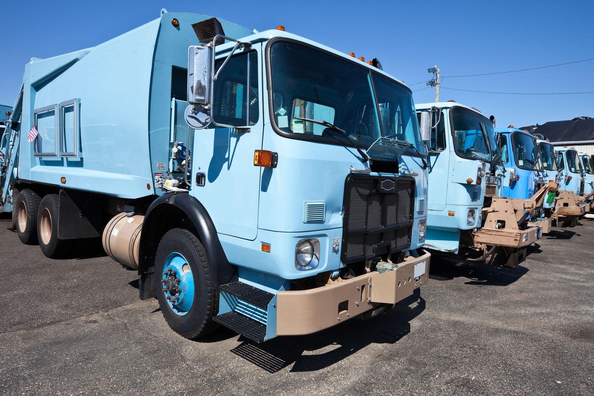 A row of blue garbage trucks are parked in a parking lot.