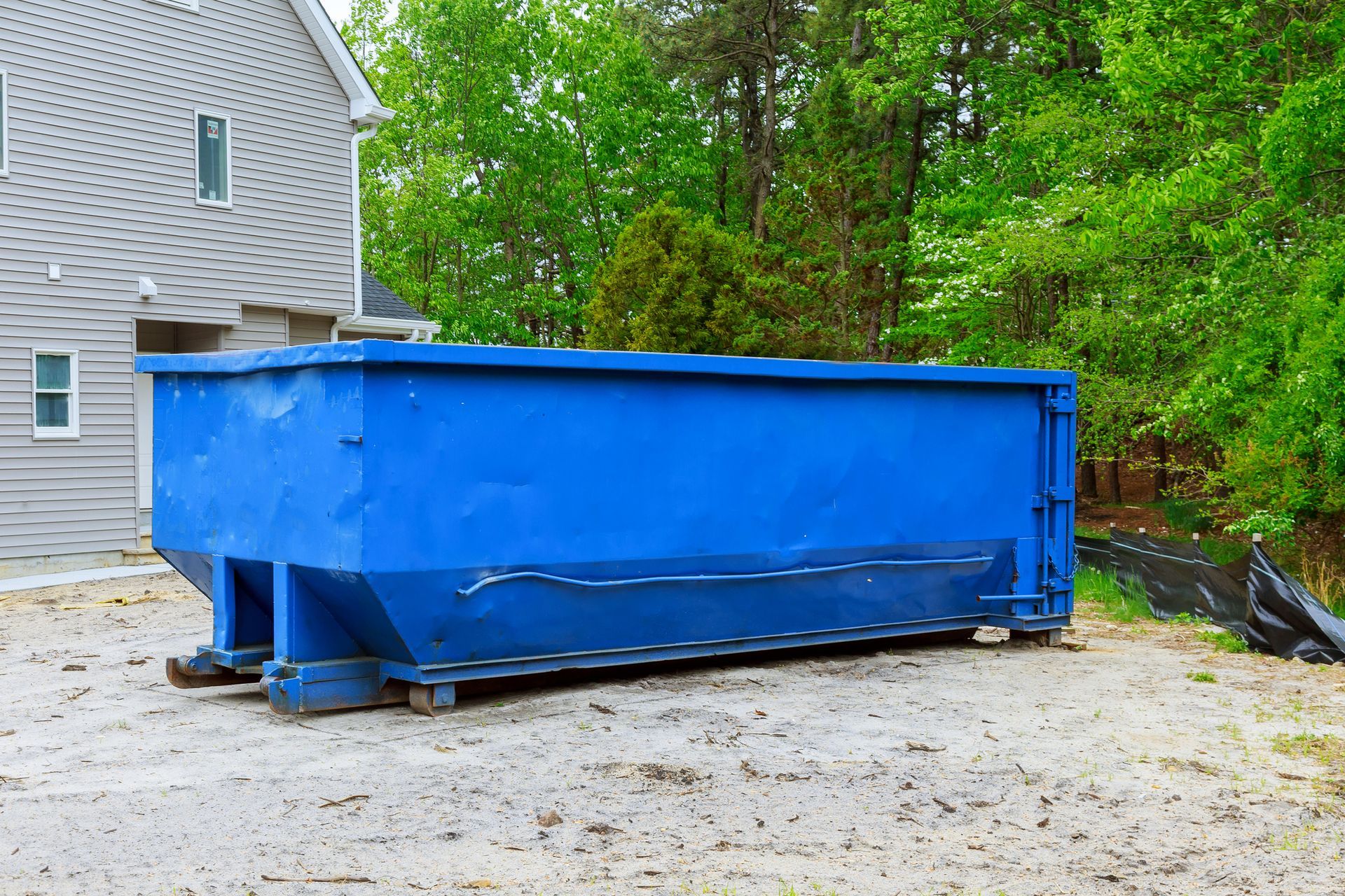 A large blue dumpster is parked in front of a house.