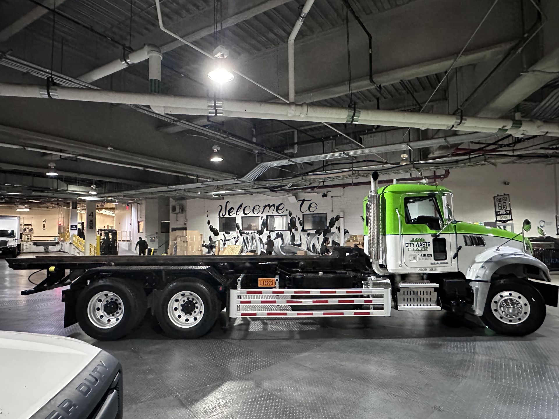 A green and white flatbed truck is parked in a garage.