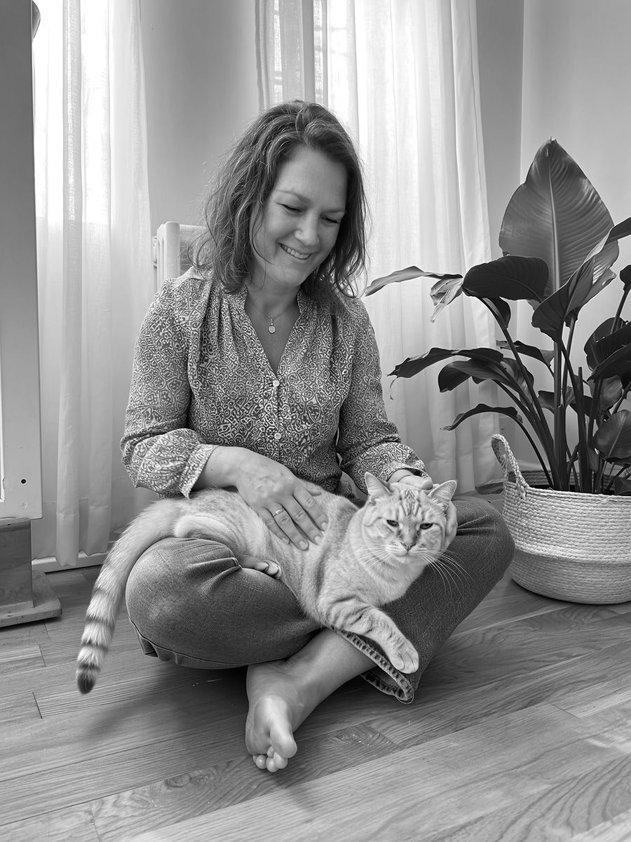 A woman is sitting on the floor petting a cat.