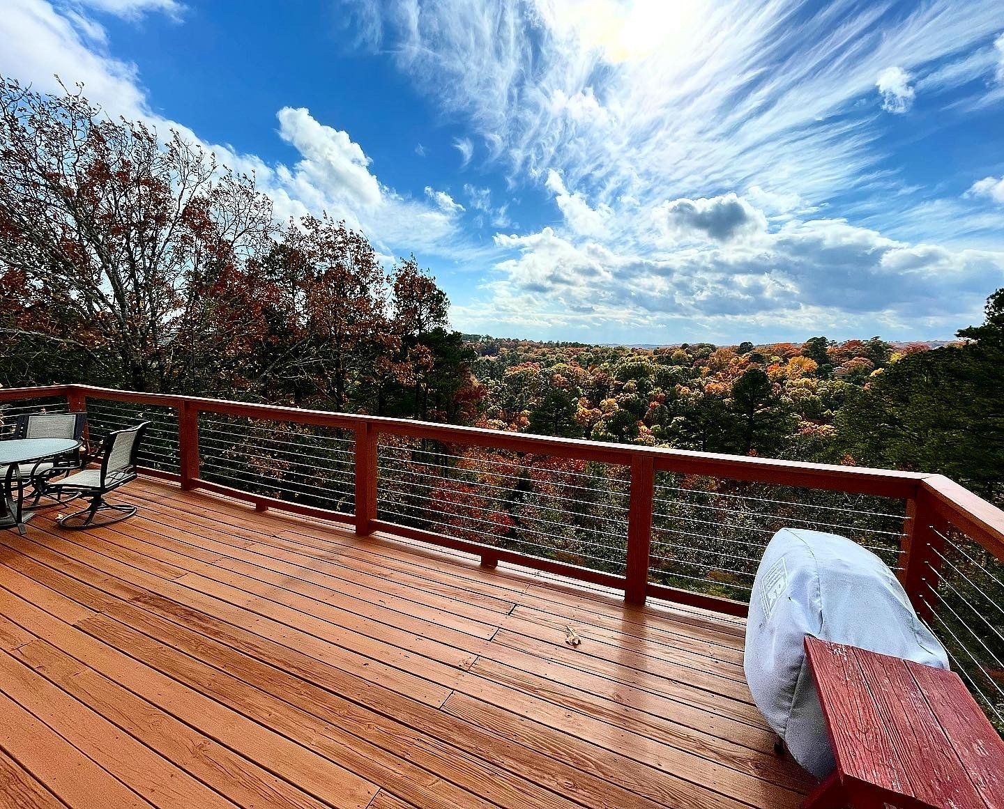 Wooden deck overlooking autumn trees and a blue sky with clouds.