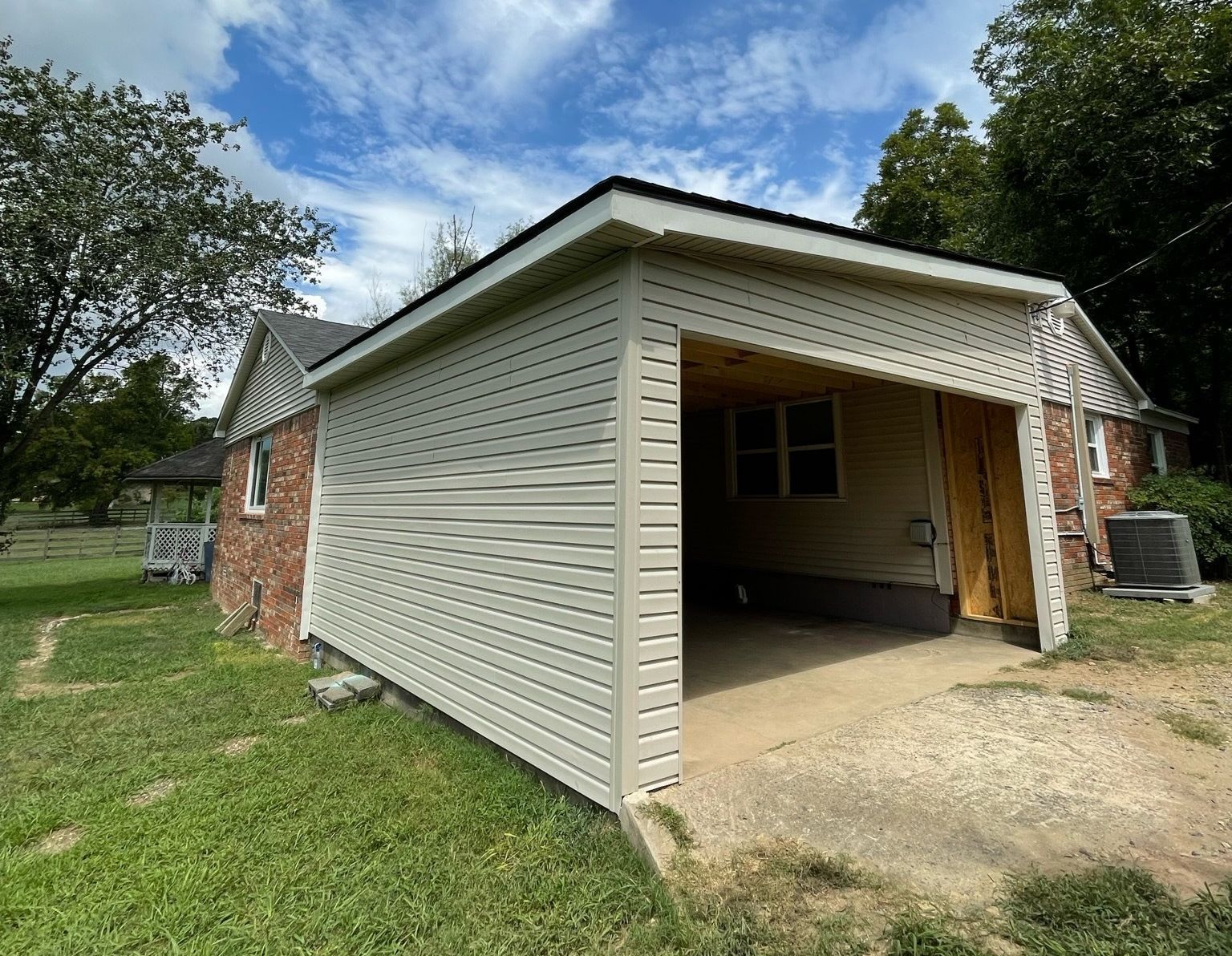 House with brick and siding, a carport, and green yard under a partly cloudy sky.