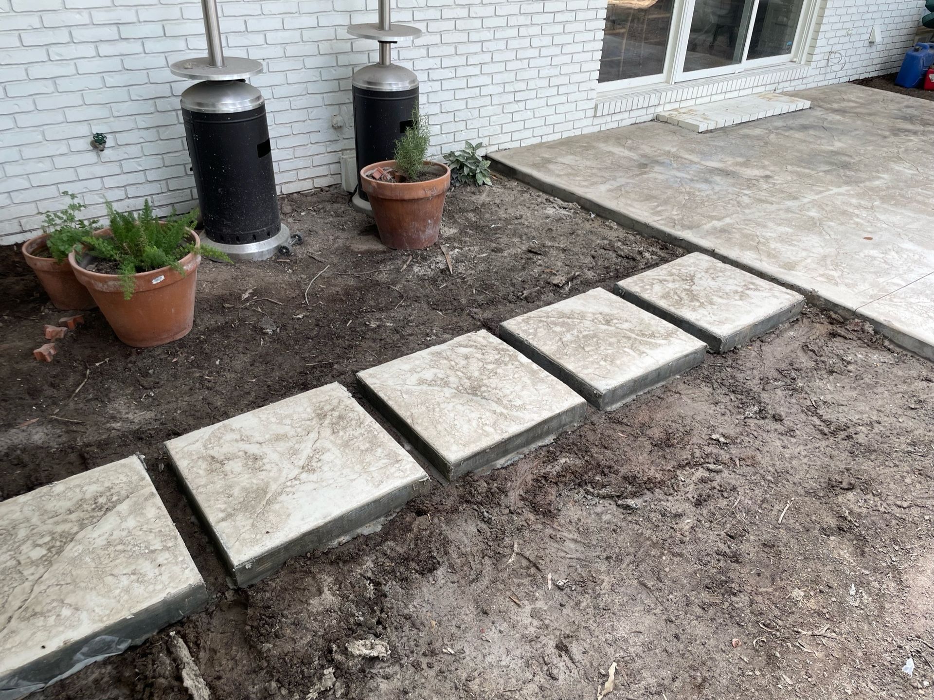 Five square stepping stones on dirt path leading to concrete patio.