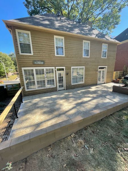 Back of a two-story beige house with a stone patio. Two doors and several windows visible.