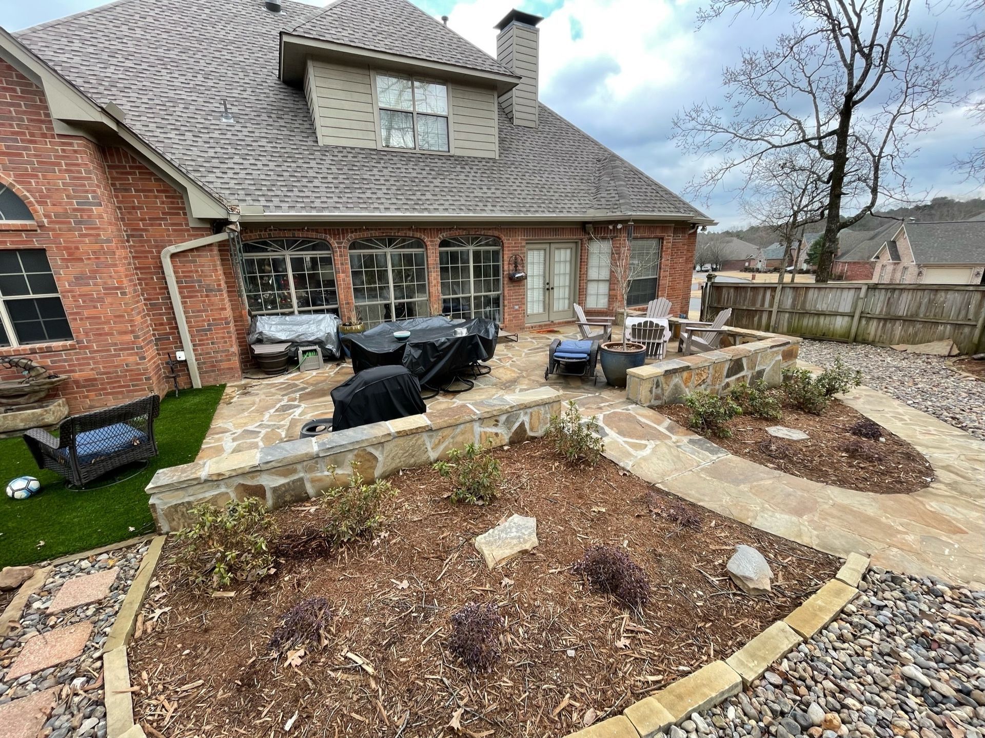 Backyard patio with brick house, flagstone, landscaping beds, and a grill.