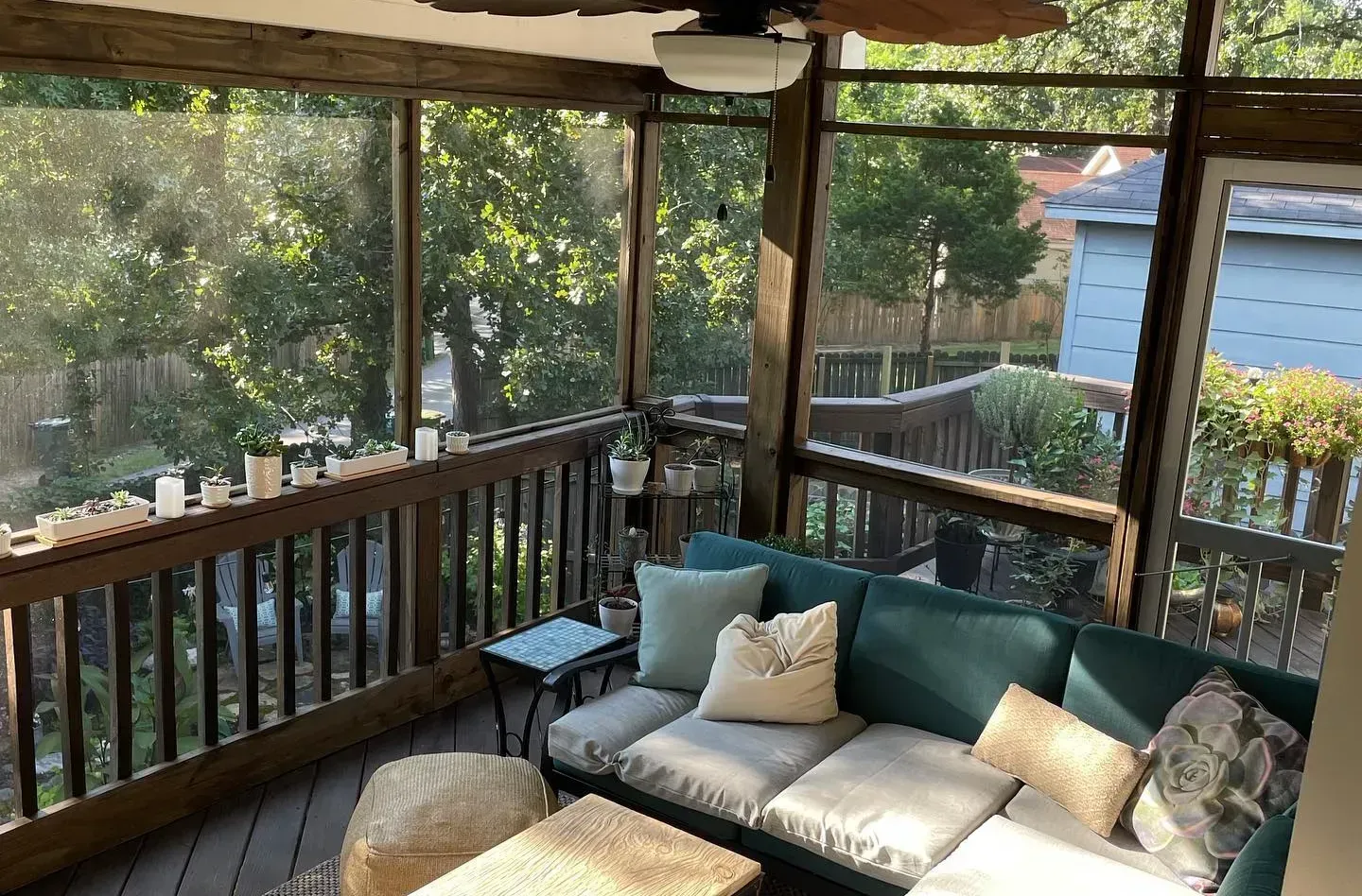Screened-in porch with teal sectional sofa, wood railing, and view of trees and deck.