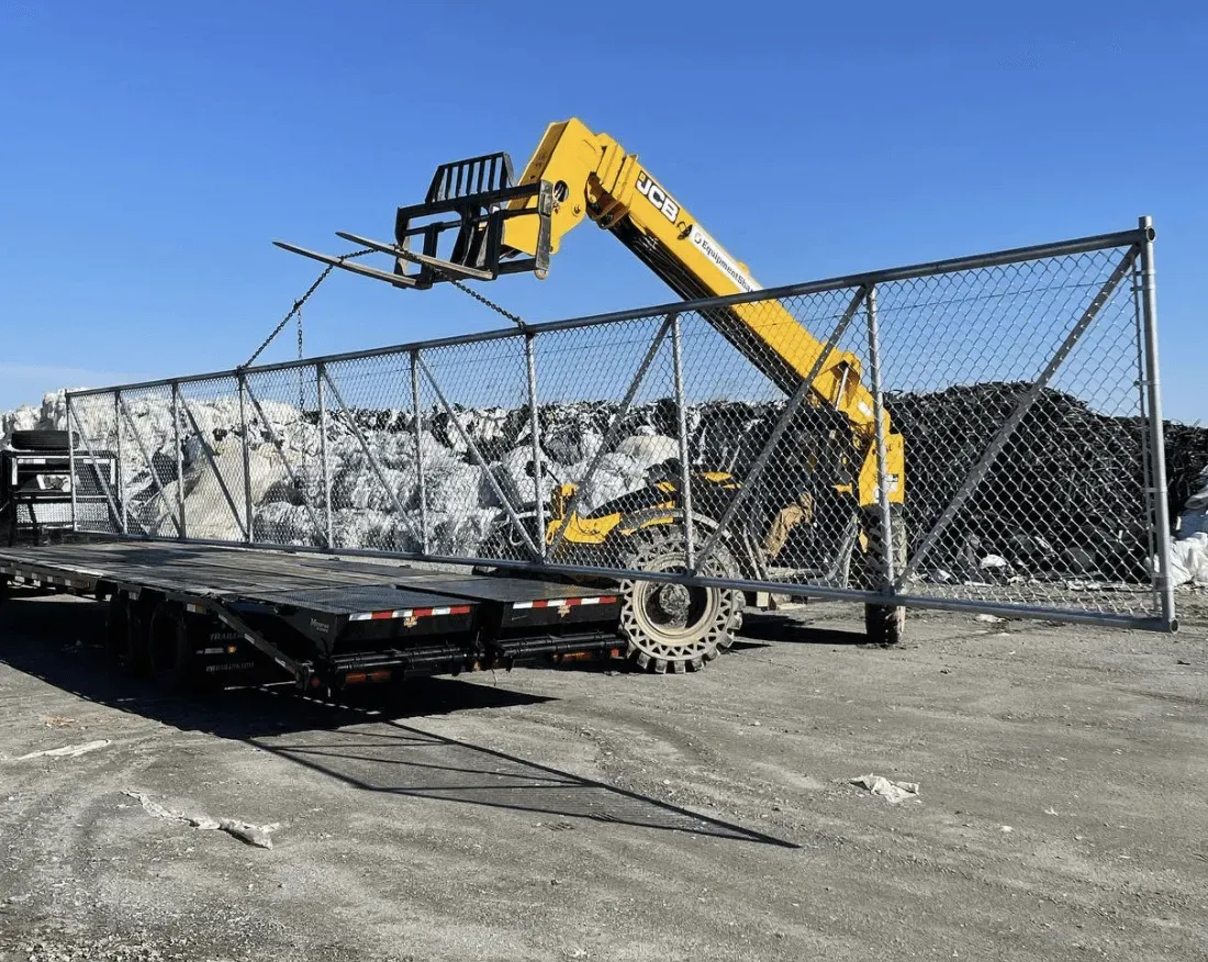 A yellow crane is lifting a fence in a parking lot.