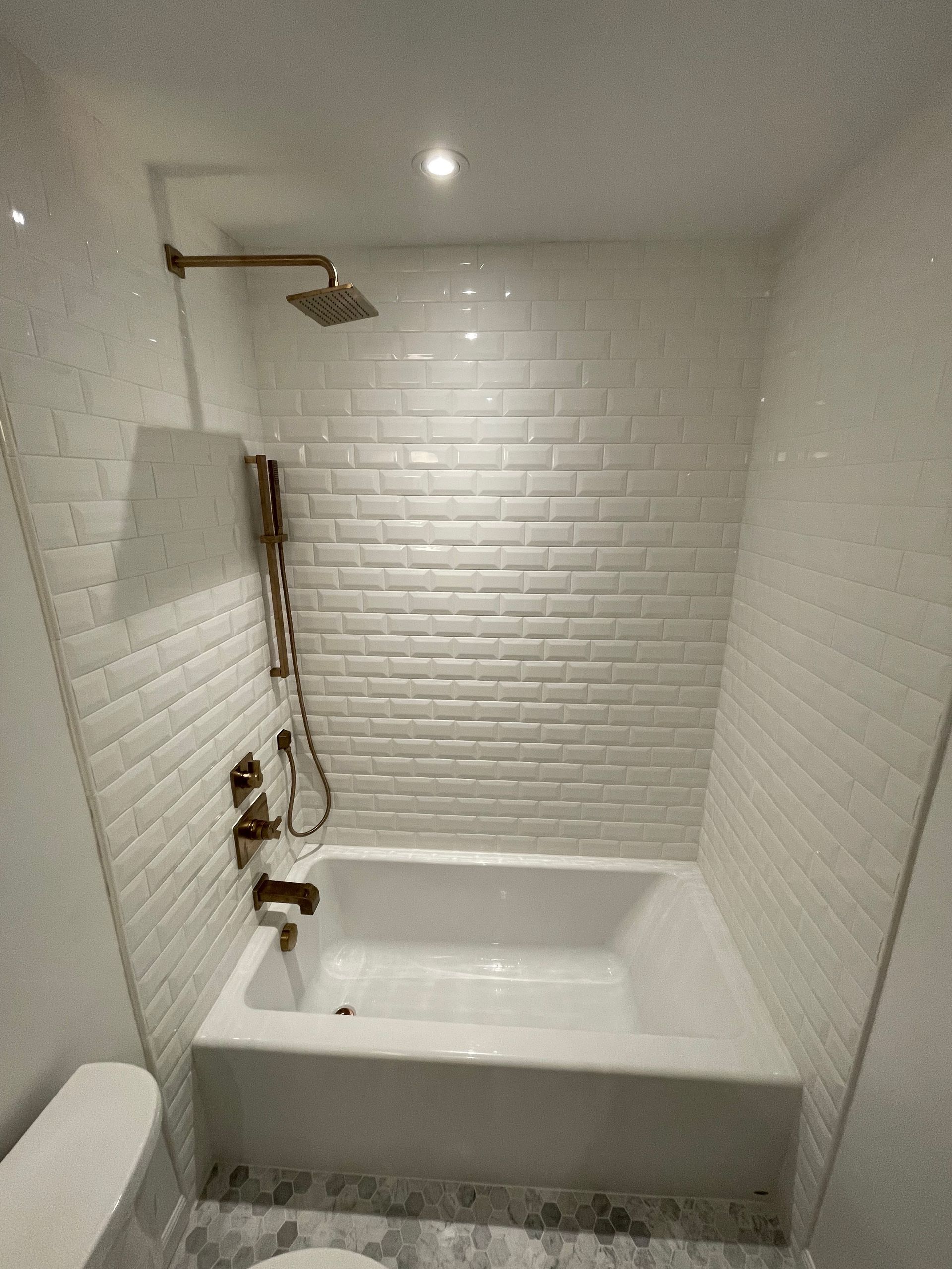 White tiled bathroom with a bathtub, showerhead, and fixtures.