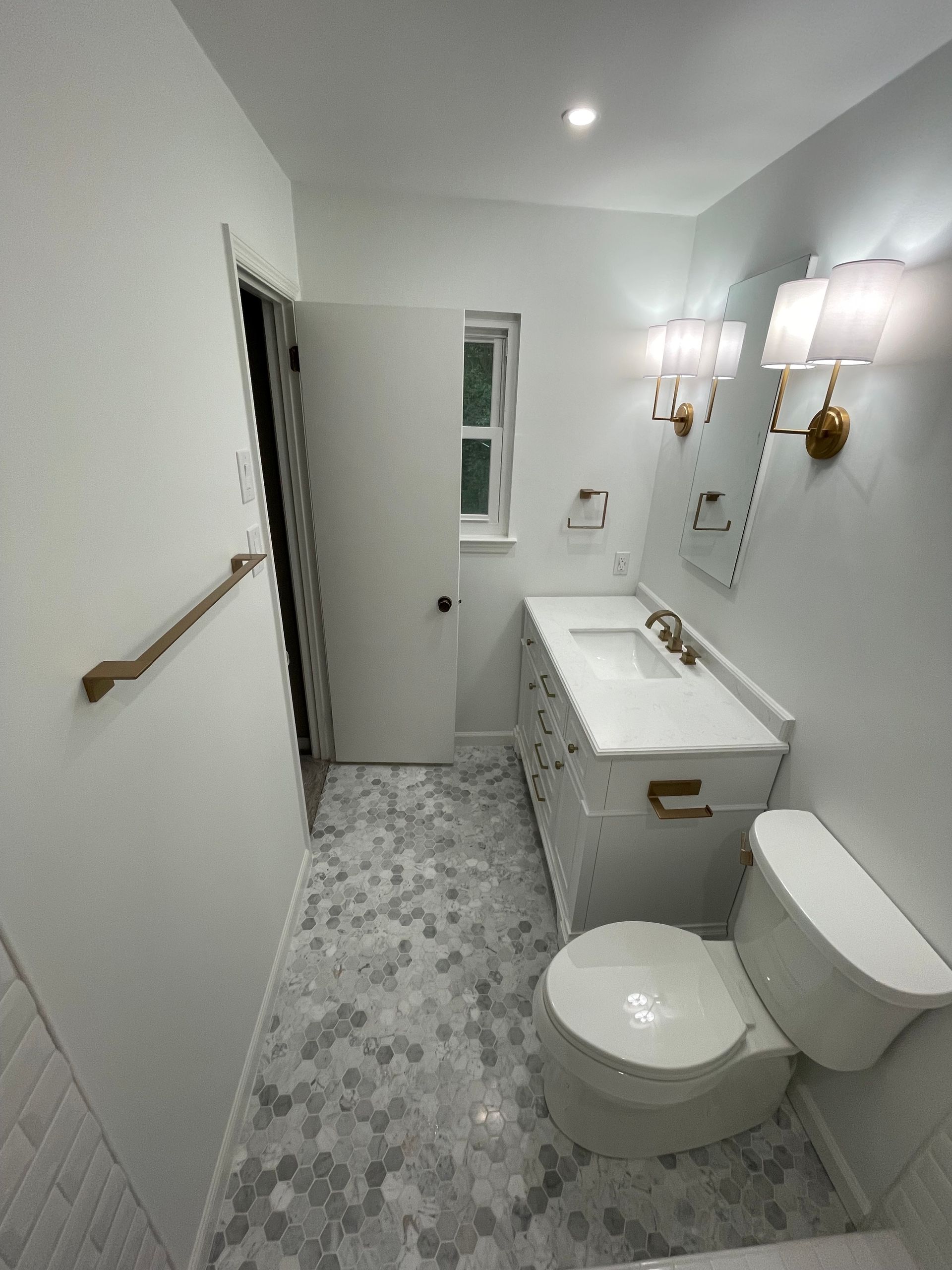 White bathroom with gray hexagon tile floor, vanity, toilet, and gold accents.