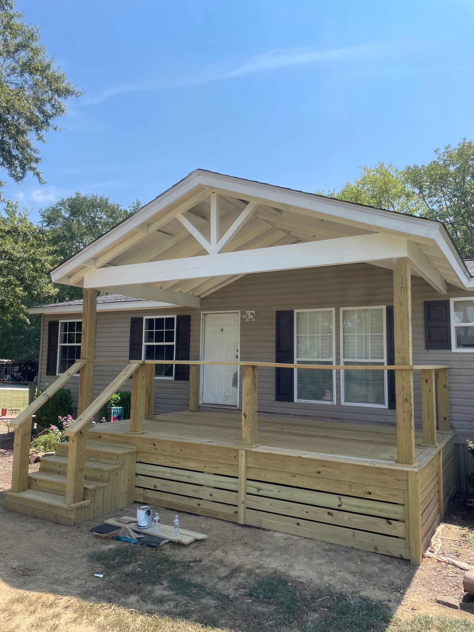 New wooden porch with a covered entry on a tan house under a blue sky.