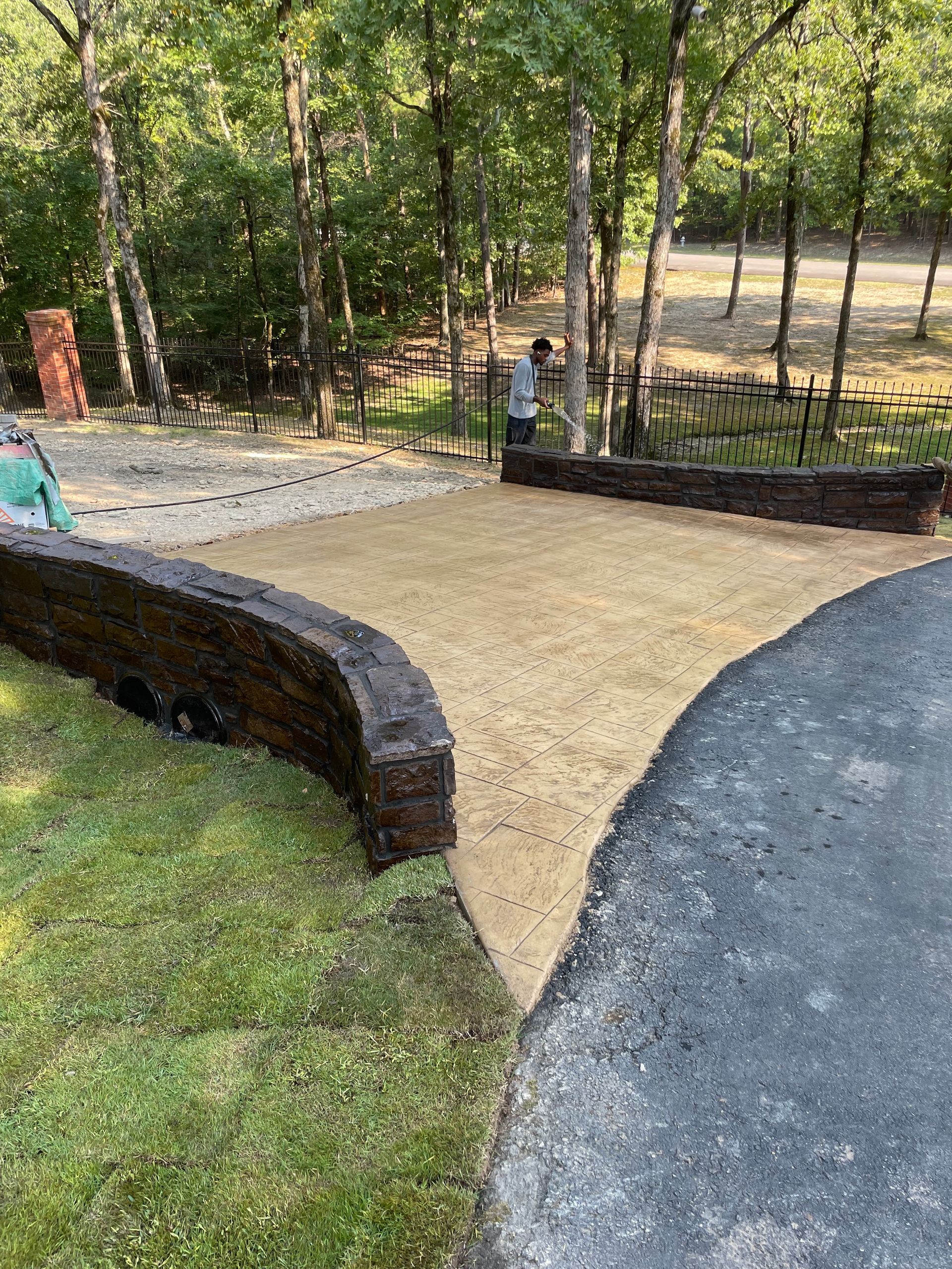 A gravel path bordered by wood and grass, connecting to asphalt. A person stands near a gate.