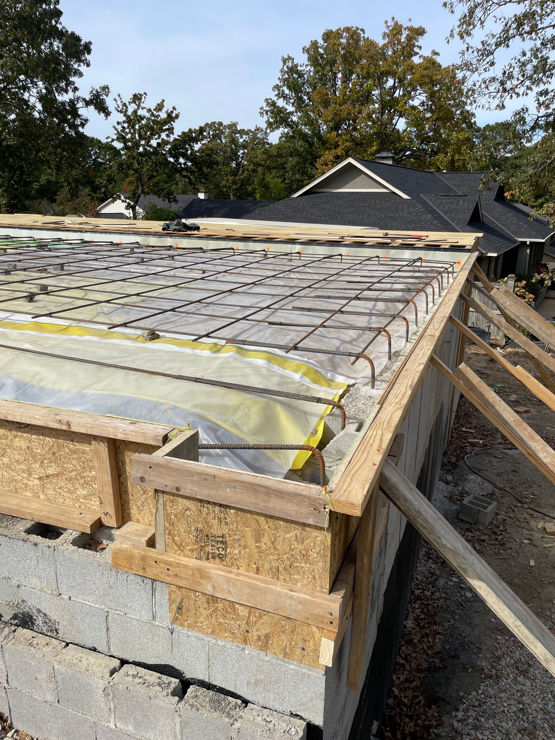 Construction site: Concrete foundation with rebar, wooden formwork, and insulation; trees in the background.
