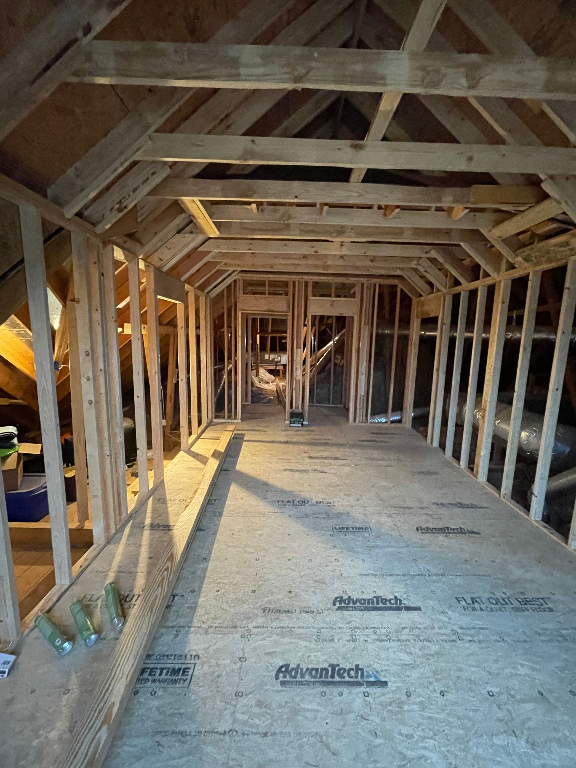 Interior view of unfinished attic with wood framing, open ceiling and walls, and plywood floor.
