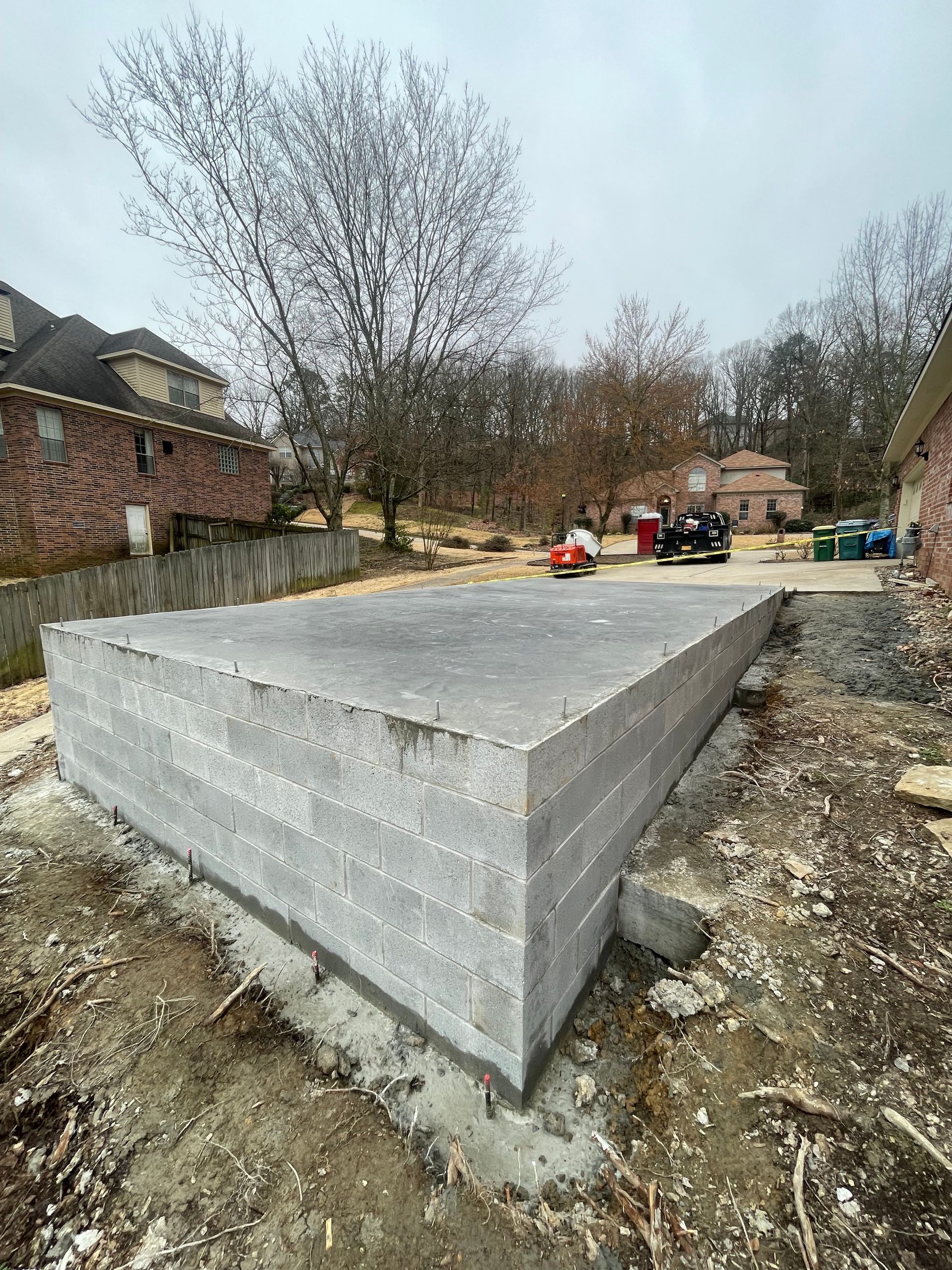 Concrete block foundation in progress, outdoors. Gray blocks on concrete base, surrounding dirt.
