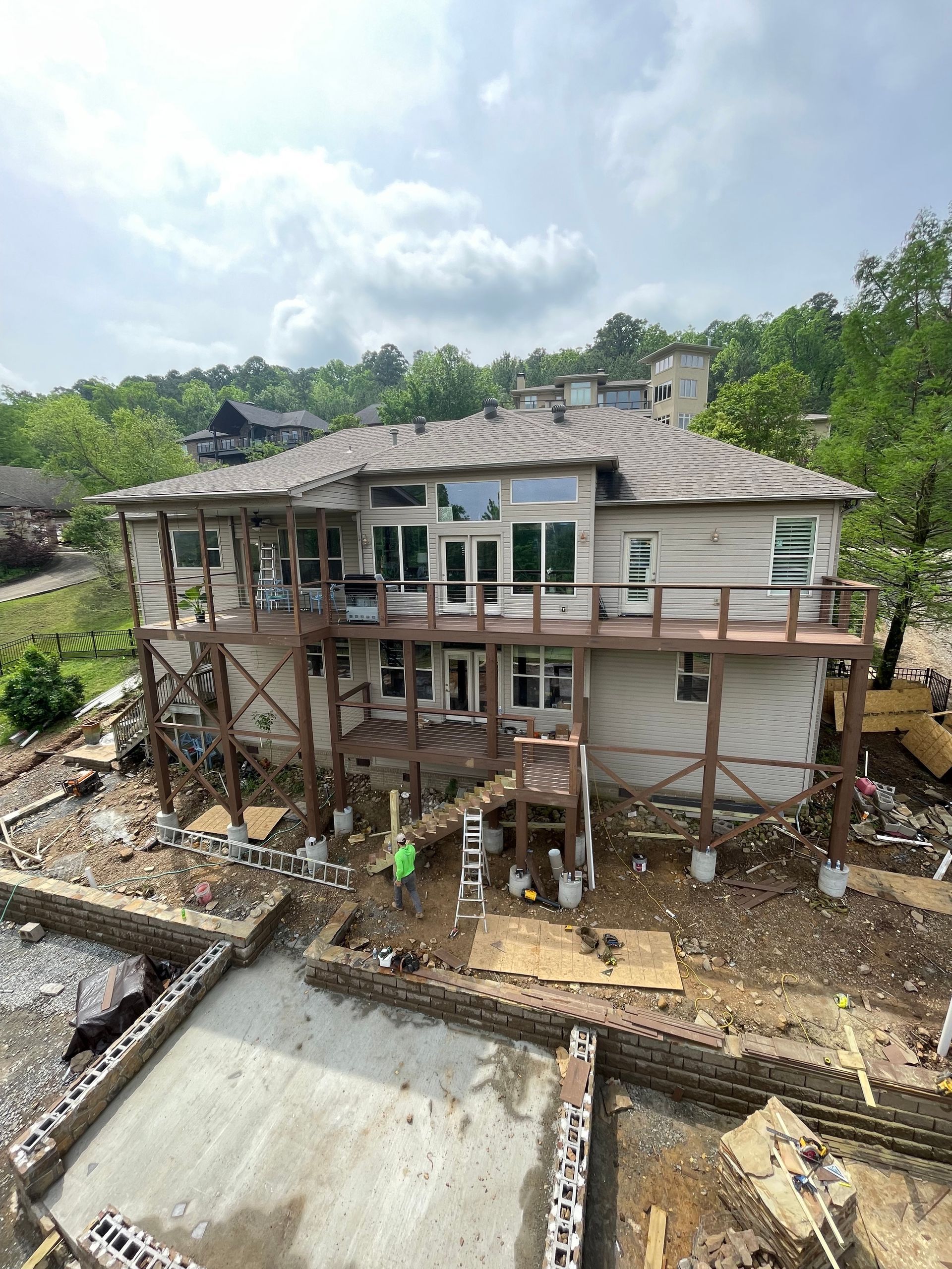House under construction, supported by wooden beams.  A partially built foundation is in the foreground. Overcast day.