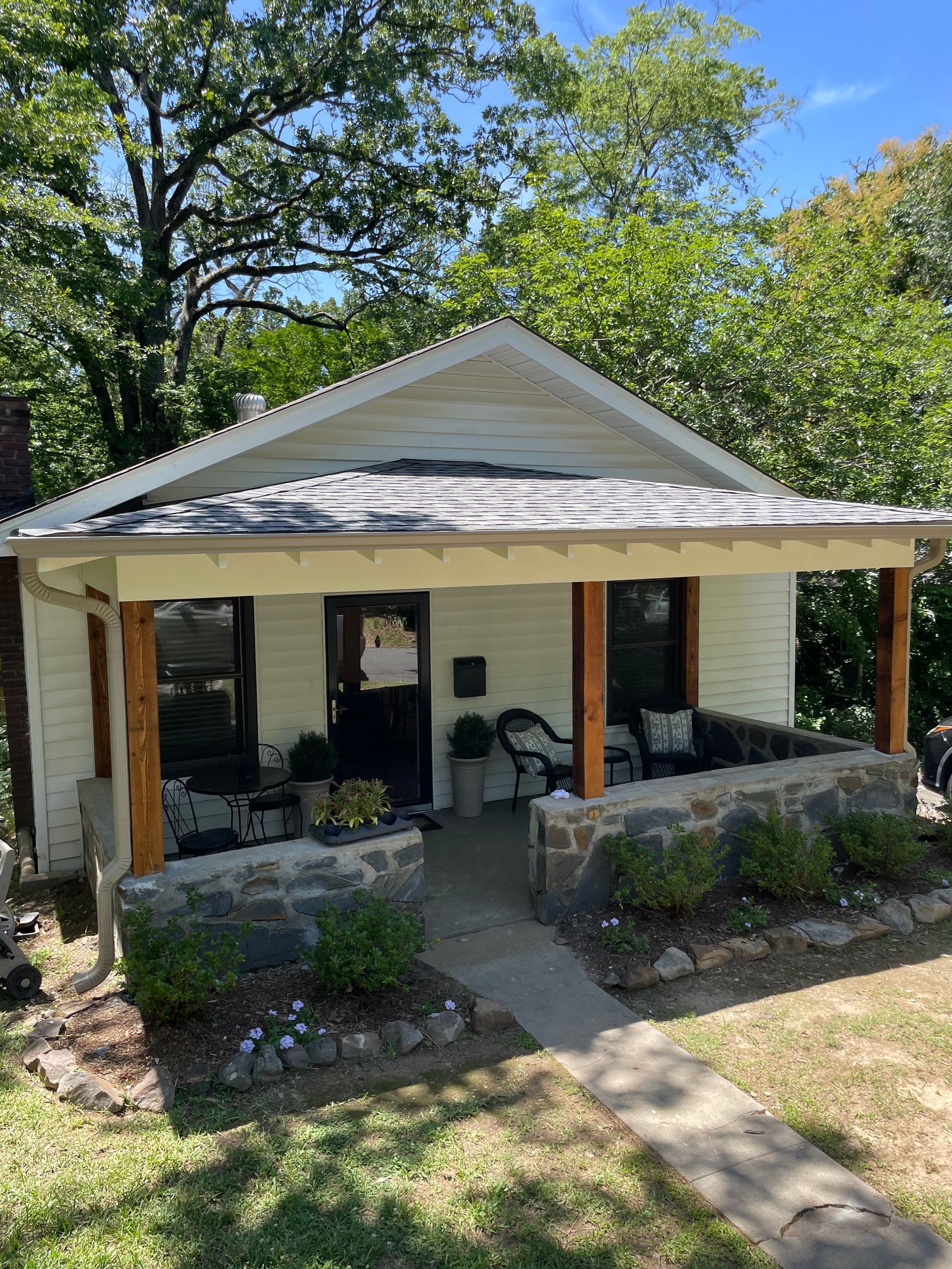 Small white house with porch, stone planters, and concrete walkway on a sunny day.