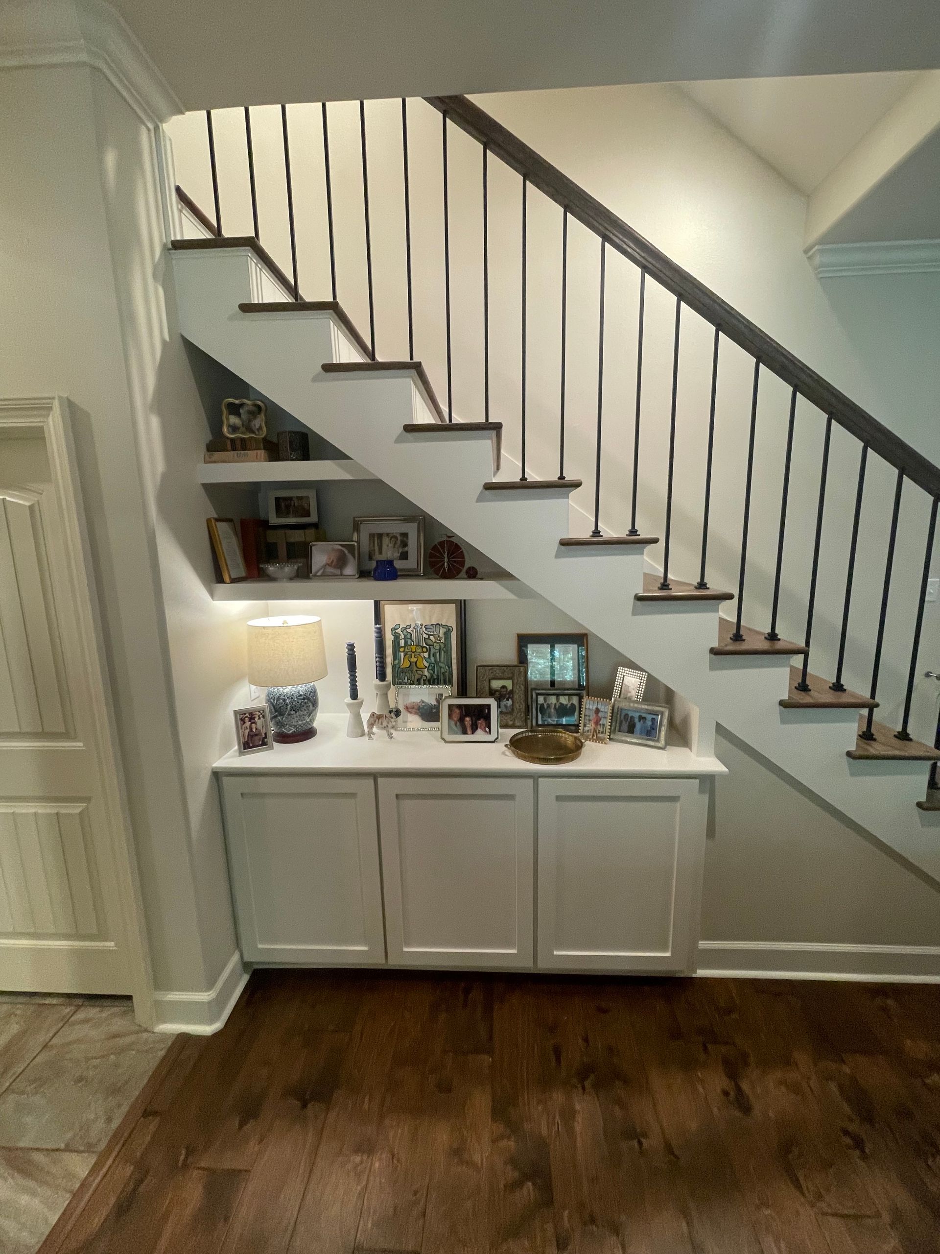 Staircase with black metal railing. White built-in cabinetry and shelves under the stairs, holding decor items.