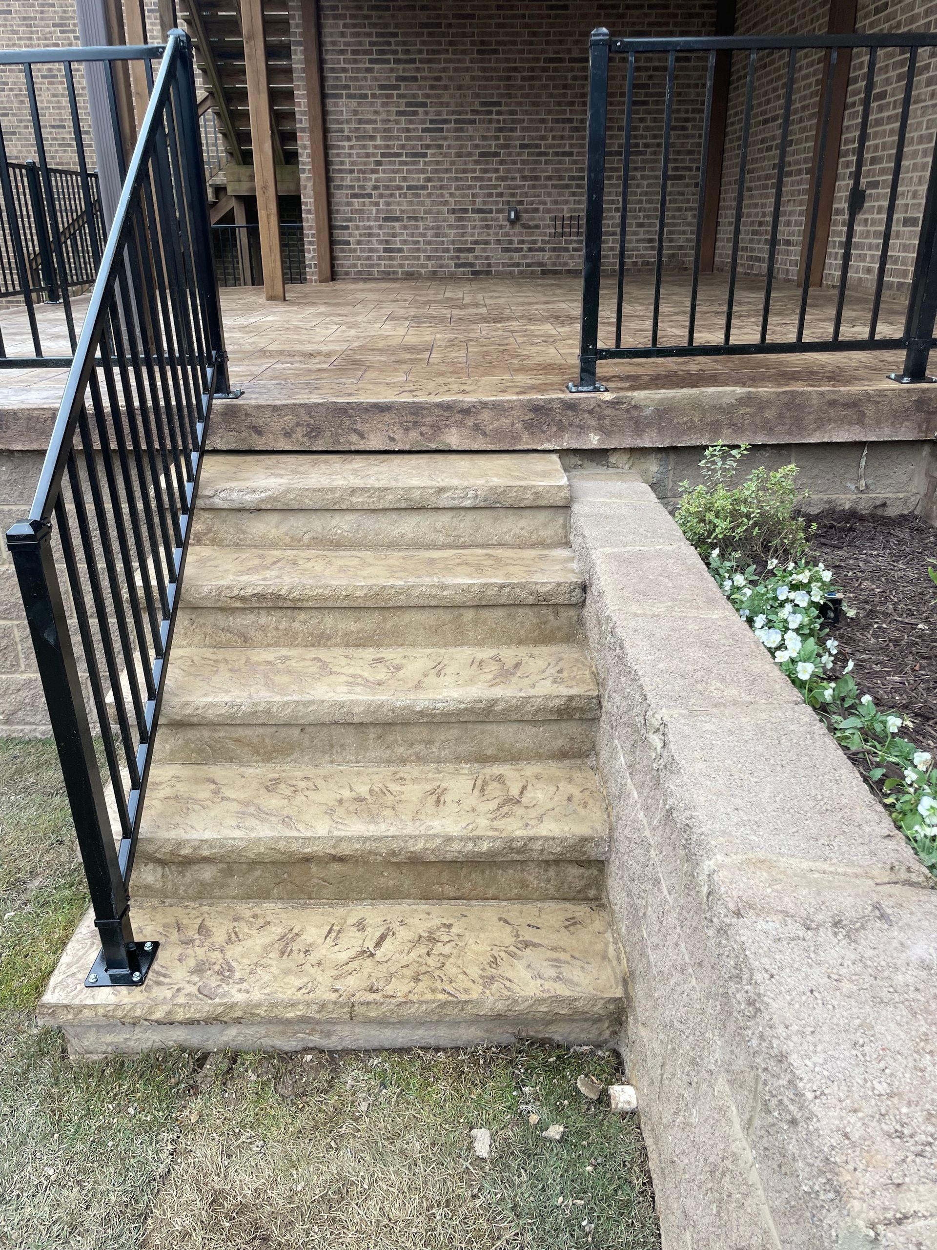Concrete outdoor steps with black handrails leading up to a landing.