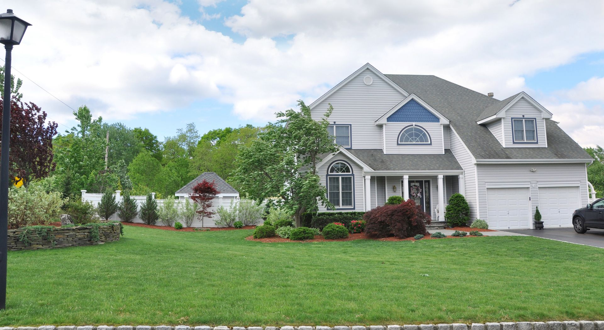 Two-story white house with a manicured lawn, landscaping, and a gray roof under a partly cloudy sky.