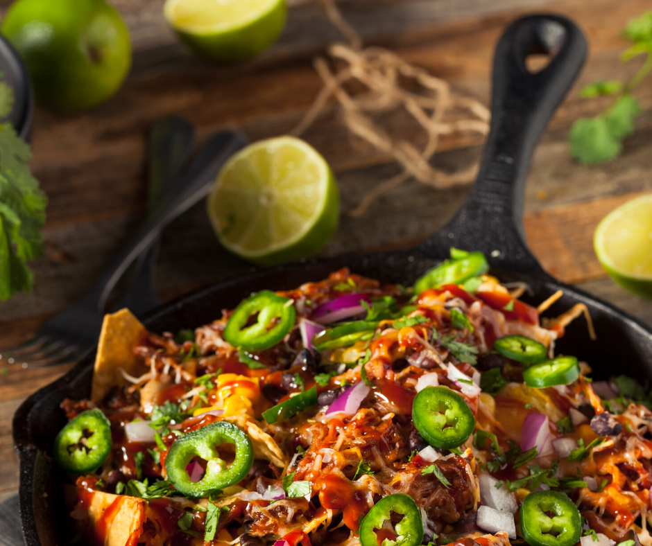 Pulled pork nachos in cast iron skillet, topped with jalapeños, onions, and lime wedges.