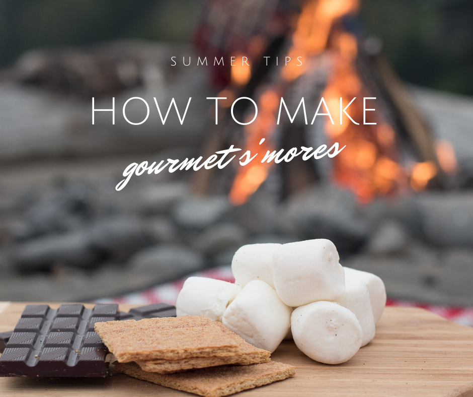 S'mores ingredients on a wooden board with a campfire in the background: graham crackers, marshmallows, and dark chocolate.
