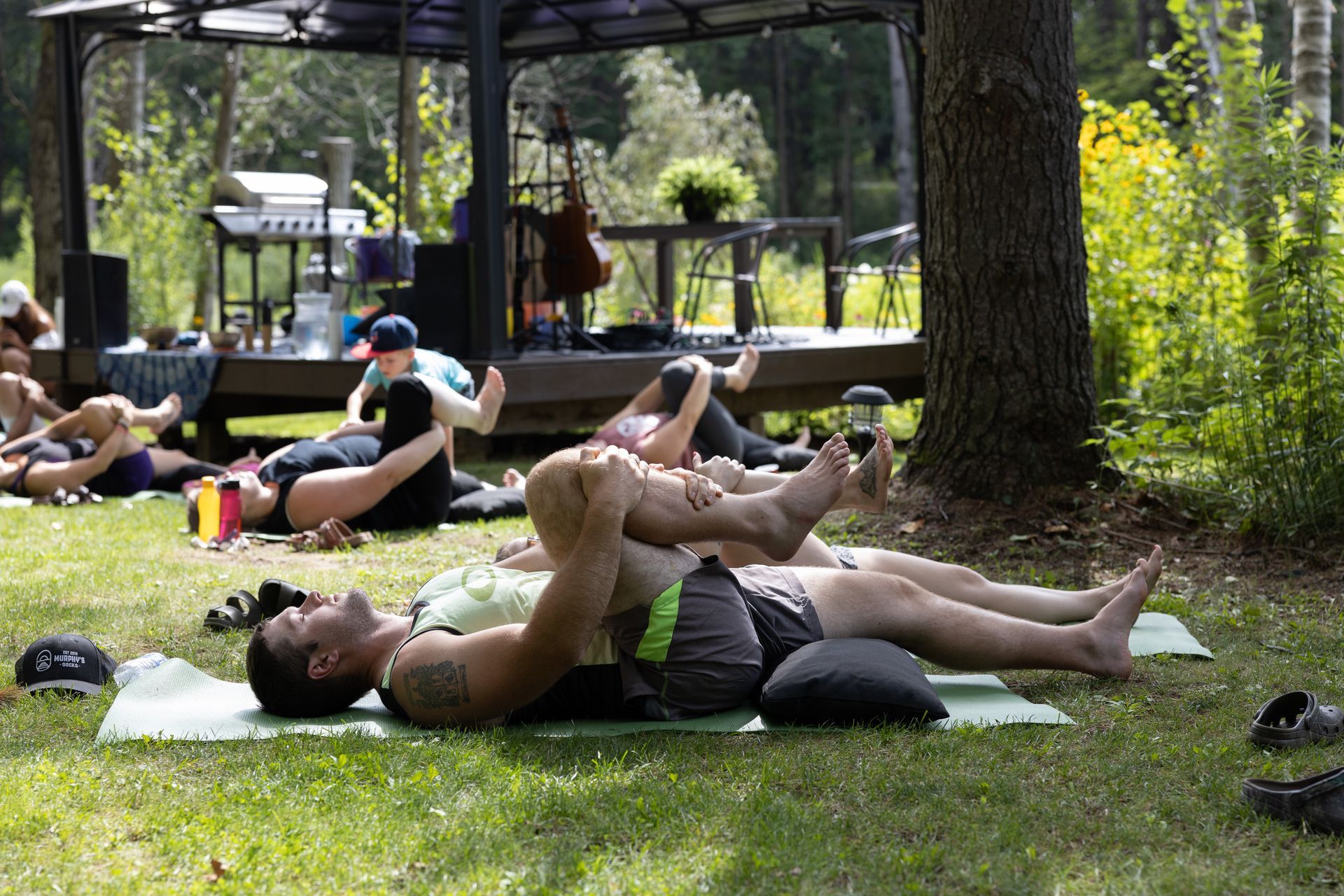 People doing yoga outdoors on grass near a gazebo.